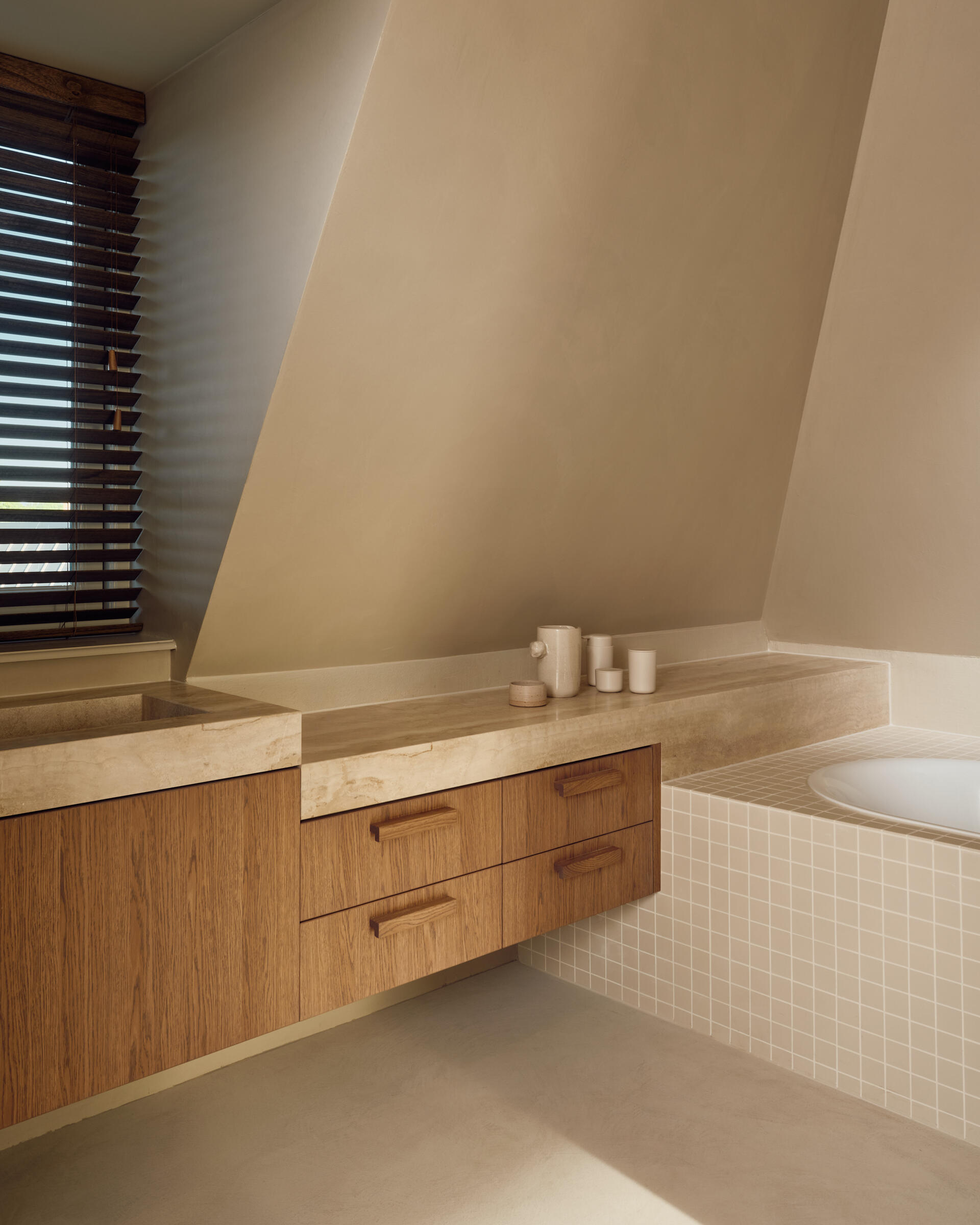 This light-filled bathroom combines travertine finishes, soft neutral tones, and peaceful views across the Rijn.