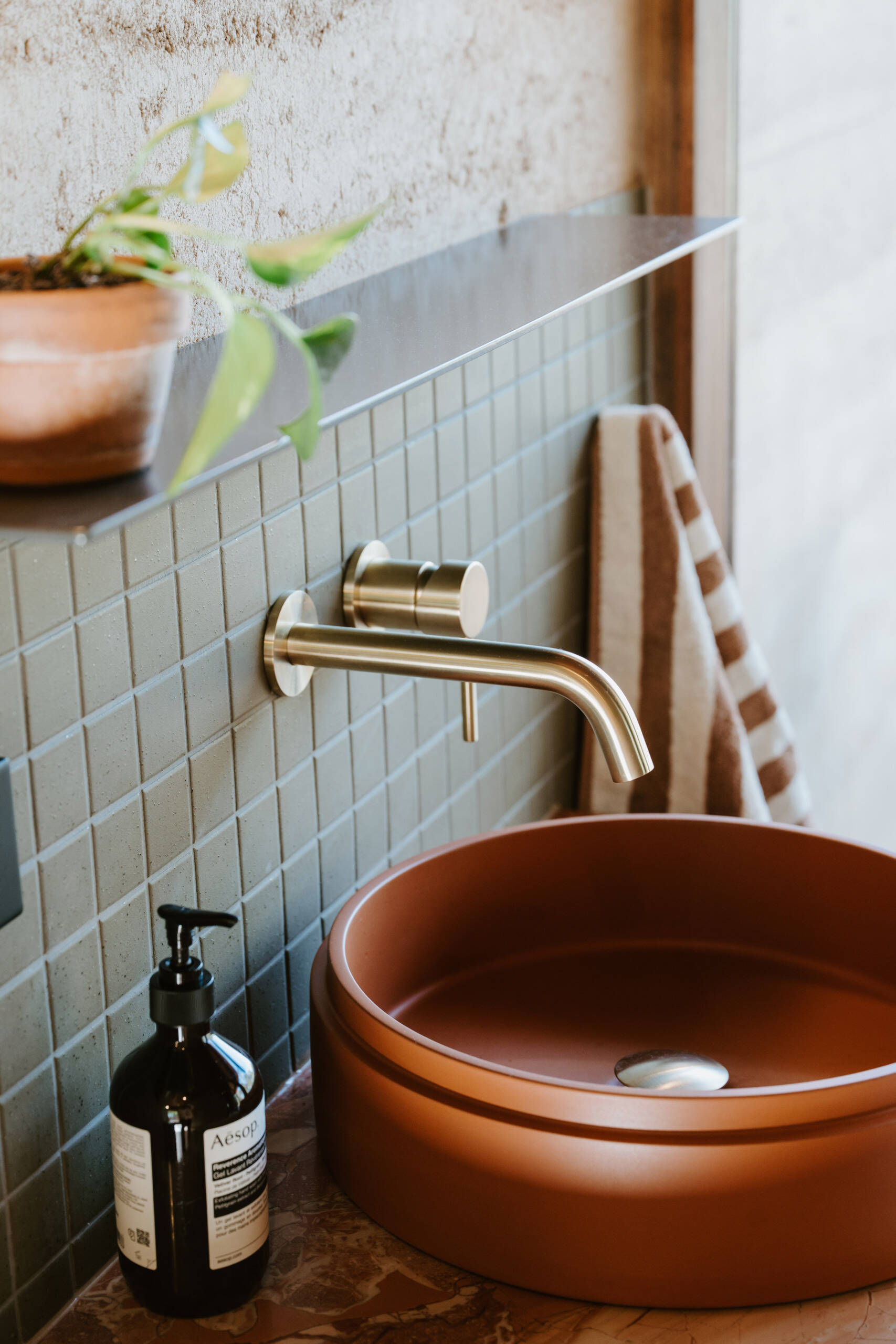 A modern off-grid cabin with rammed earth walls and sage green square tiles in the bathroom.