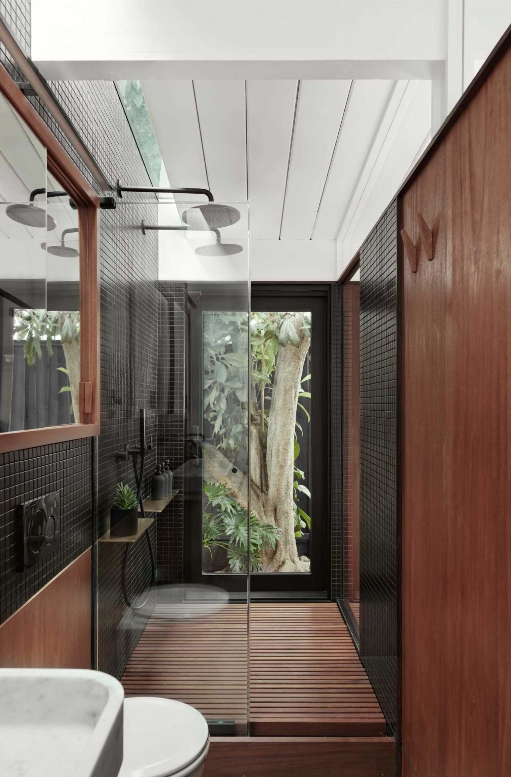 A black-on-black ensuite with mahogany cabinetry, brass accents, and matte black mosaic tiles creating a subtle, warm-toned bathroom interior in a San Jose Eichler home.