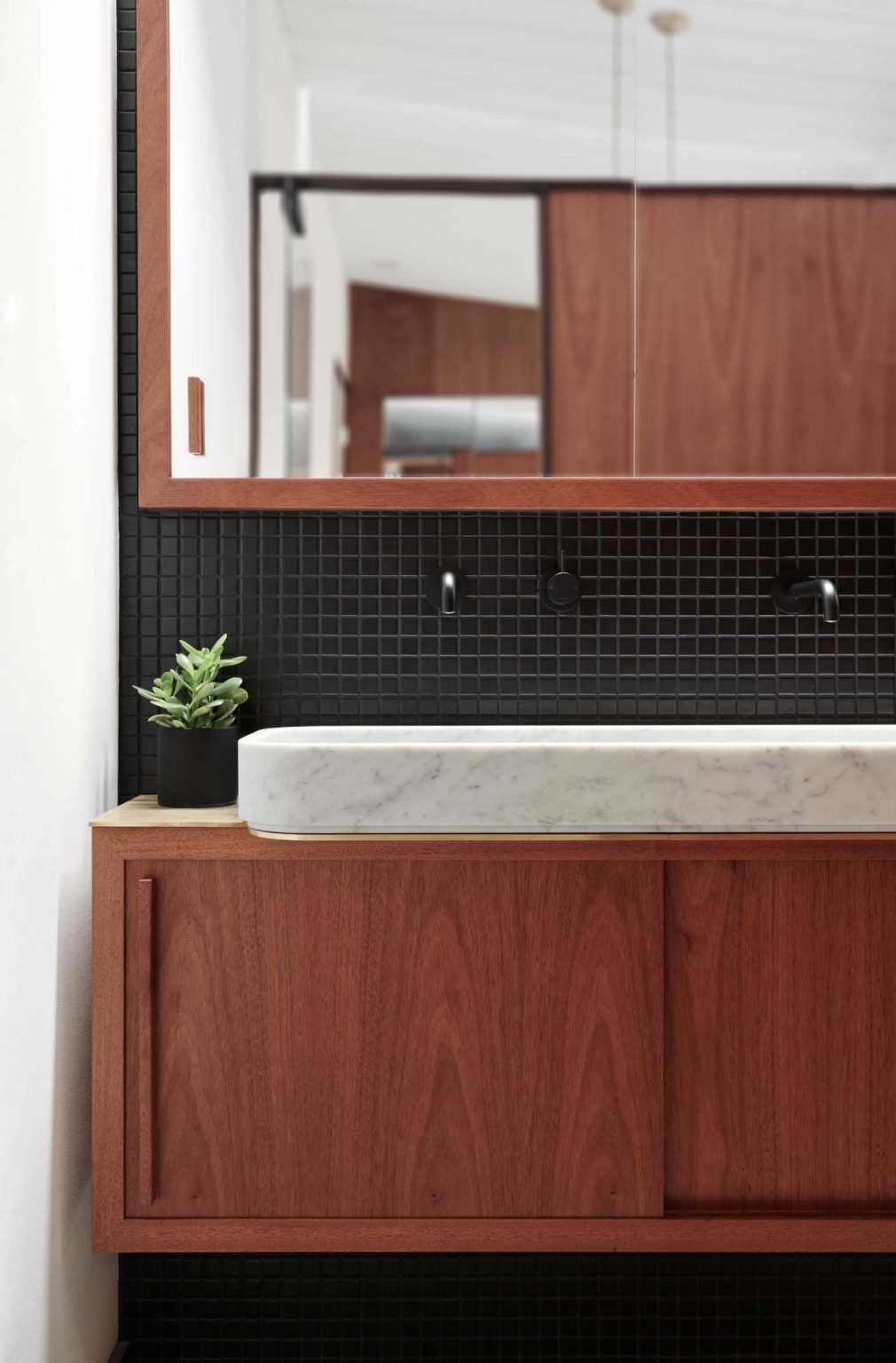 A black-on-black ensuite with mahogany cabinetry, brass accents, and matte black mosaic tiles creating a subtle, warm-toned bathroom interior in a San Jose Eichler home.