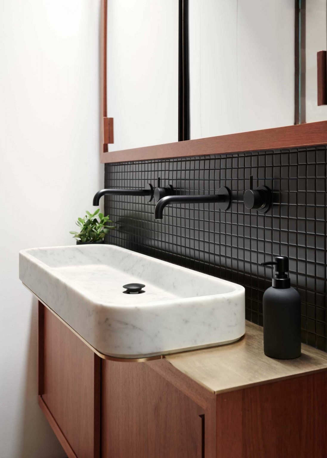 A black-on-black ensuite with mahogany cabinetry, brass accents, and matte black mosaic tiles creating a subtle, warm-toned bathroom interior in a San Jose Eichler home.
