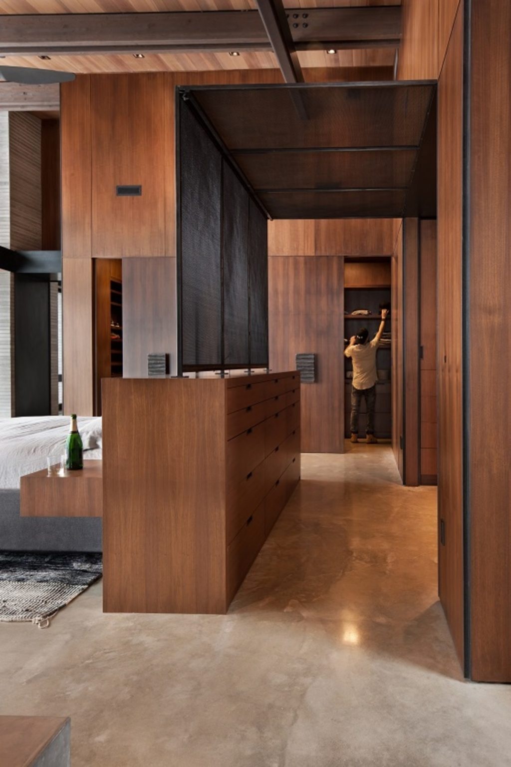 This bedroom features an unusual layout with the bed positioned in the center of the room. A multi-functional headboard doubles as a dresser, helping define the space while maintaining openness and views.