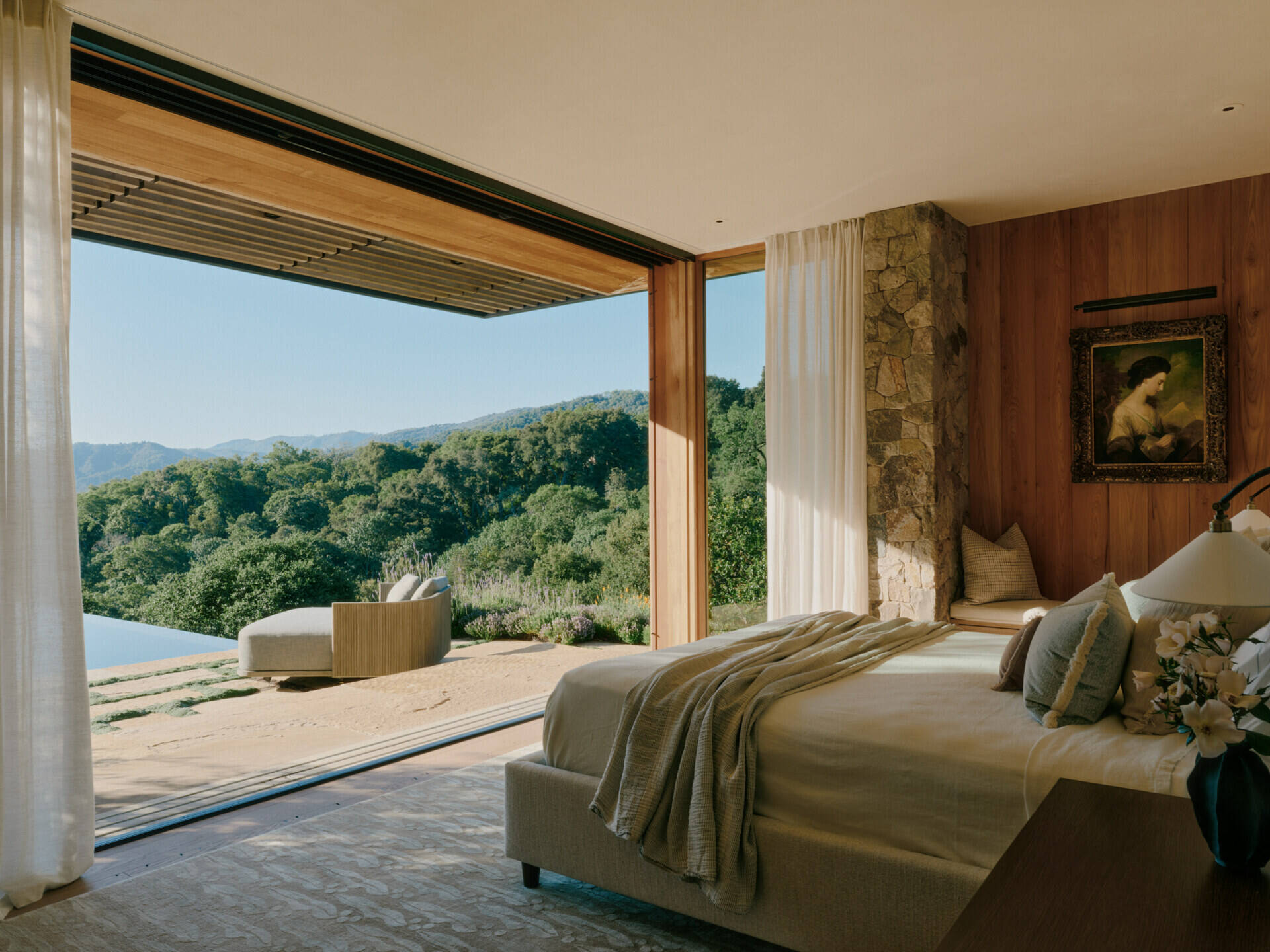 Warm stone walls, wood finishes, and panoramic preserve views create a calm modern bedroom inside Stone Villa.