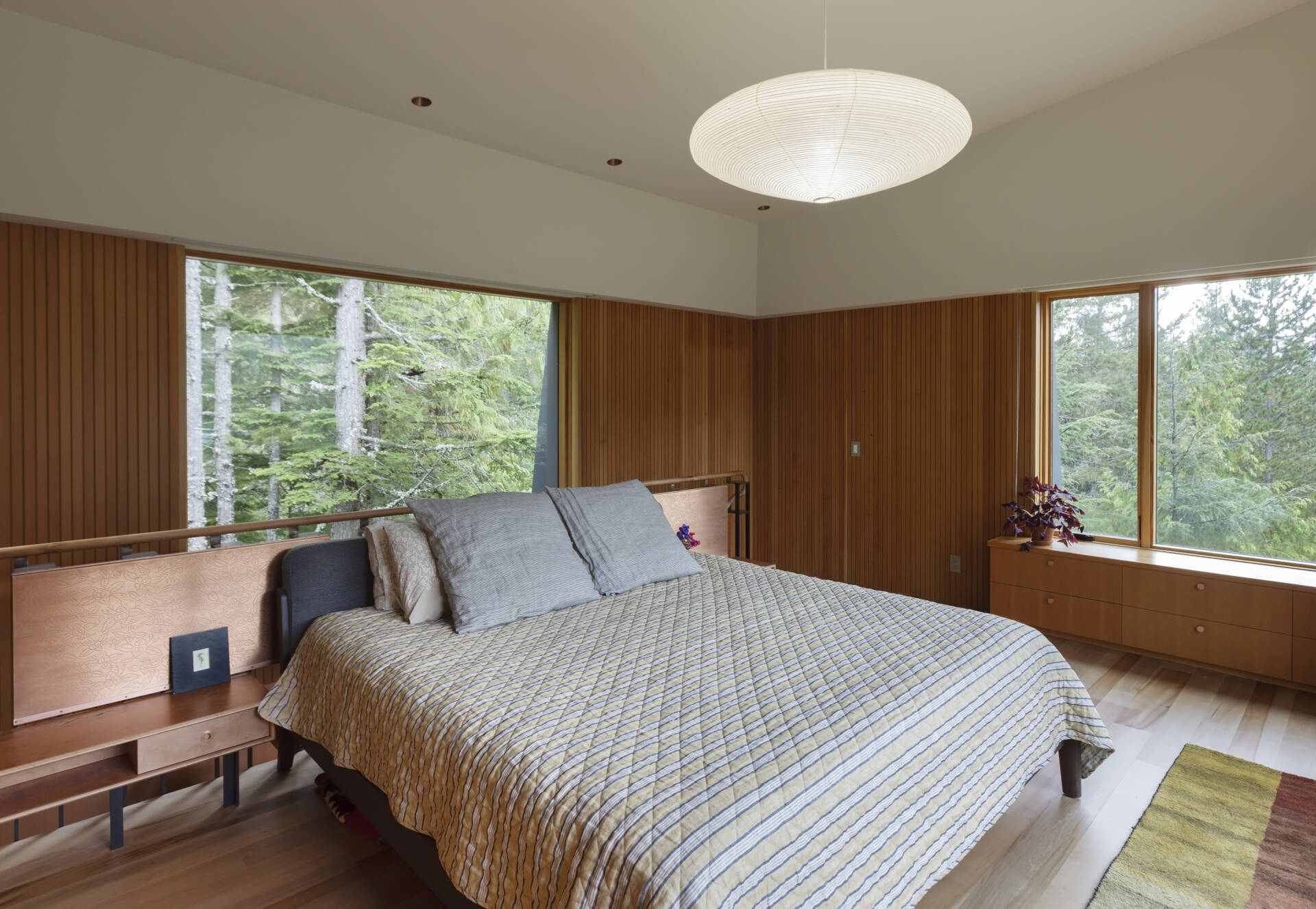 This treehouse-inspired bedroom features etched copper screens, forest views, and warm Pacific madrone wood tones.