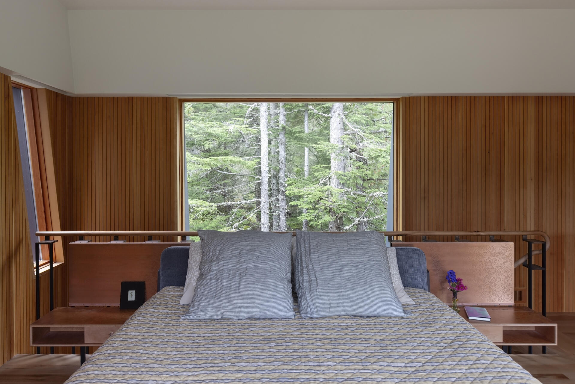 This treehouse-inspired bedroom features etched copper screens, forest views, and warm Pacific madrone wood tones.