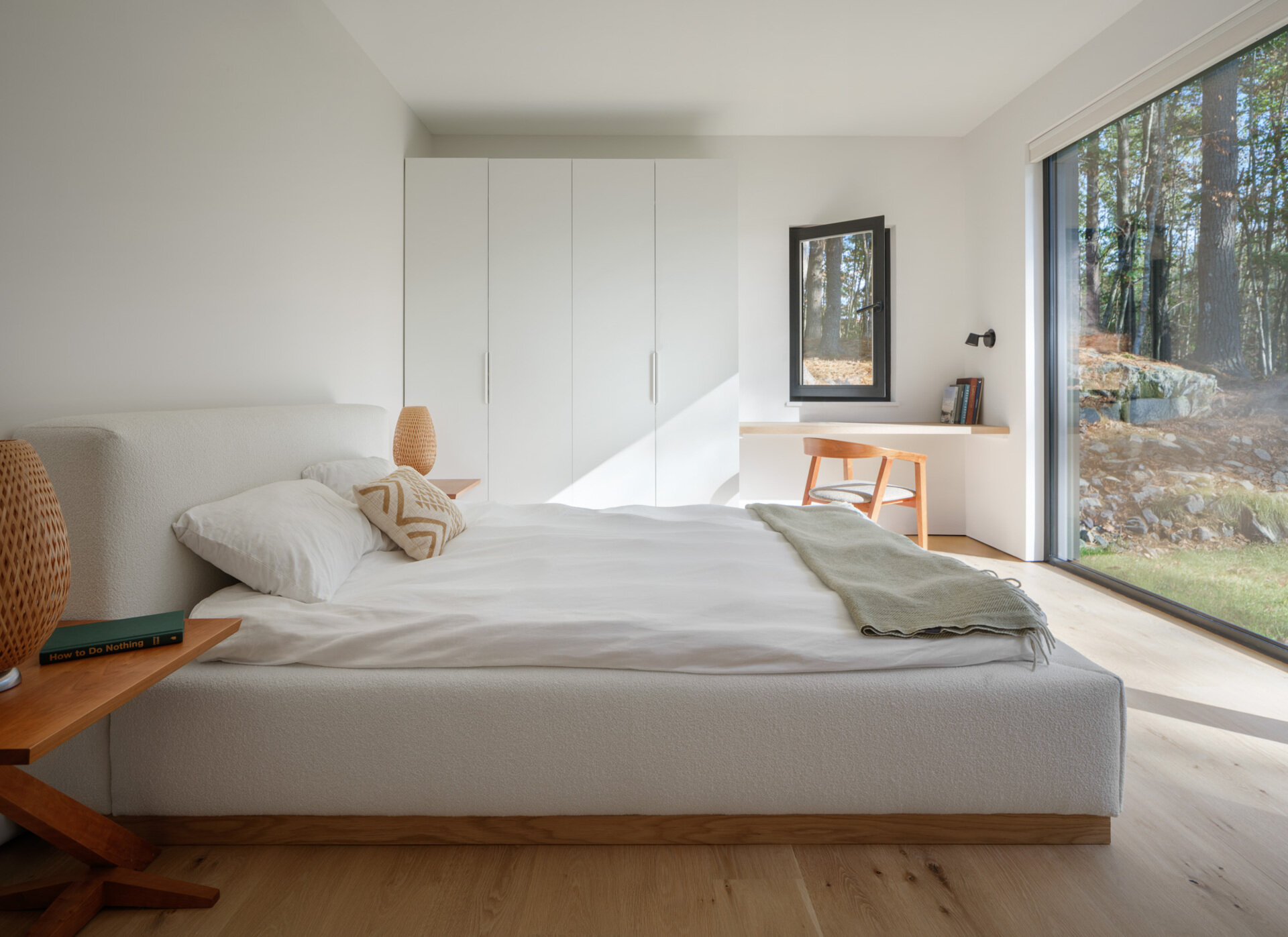A minimalist bedroom with a built-in desk and large windows creates a bright and practical space for modern living.