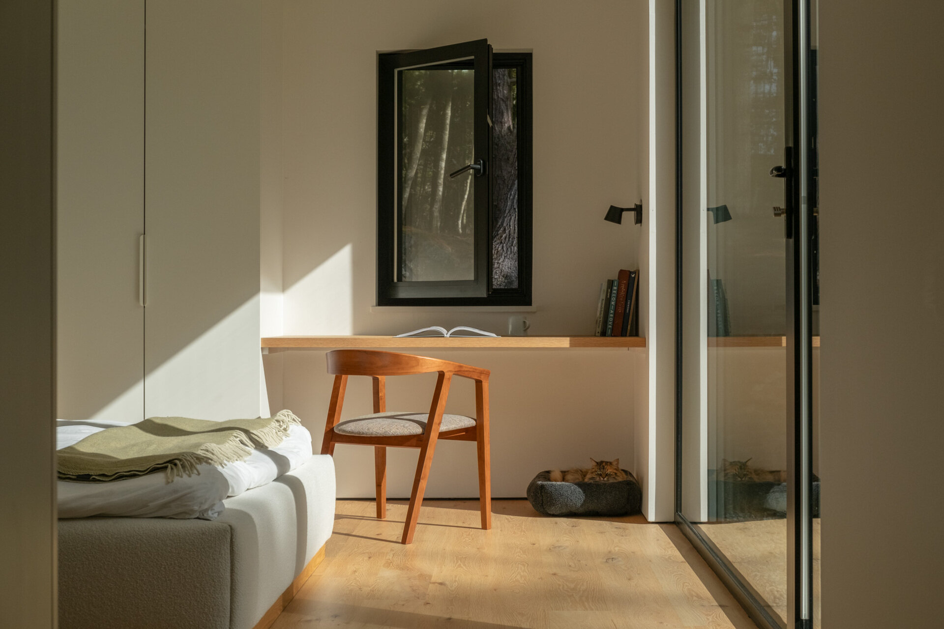A minimalist bedroom with a built-in desk and large windows creates a bright and practical space for modern living.