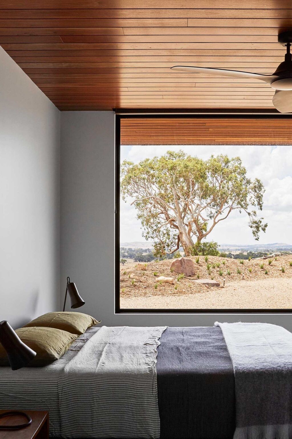 A minimalist bedroom with a large picture window framing expansive countryside views.