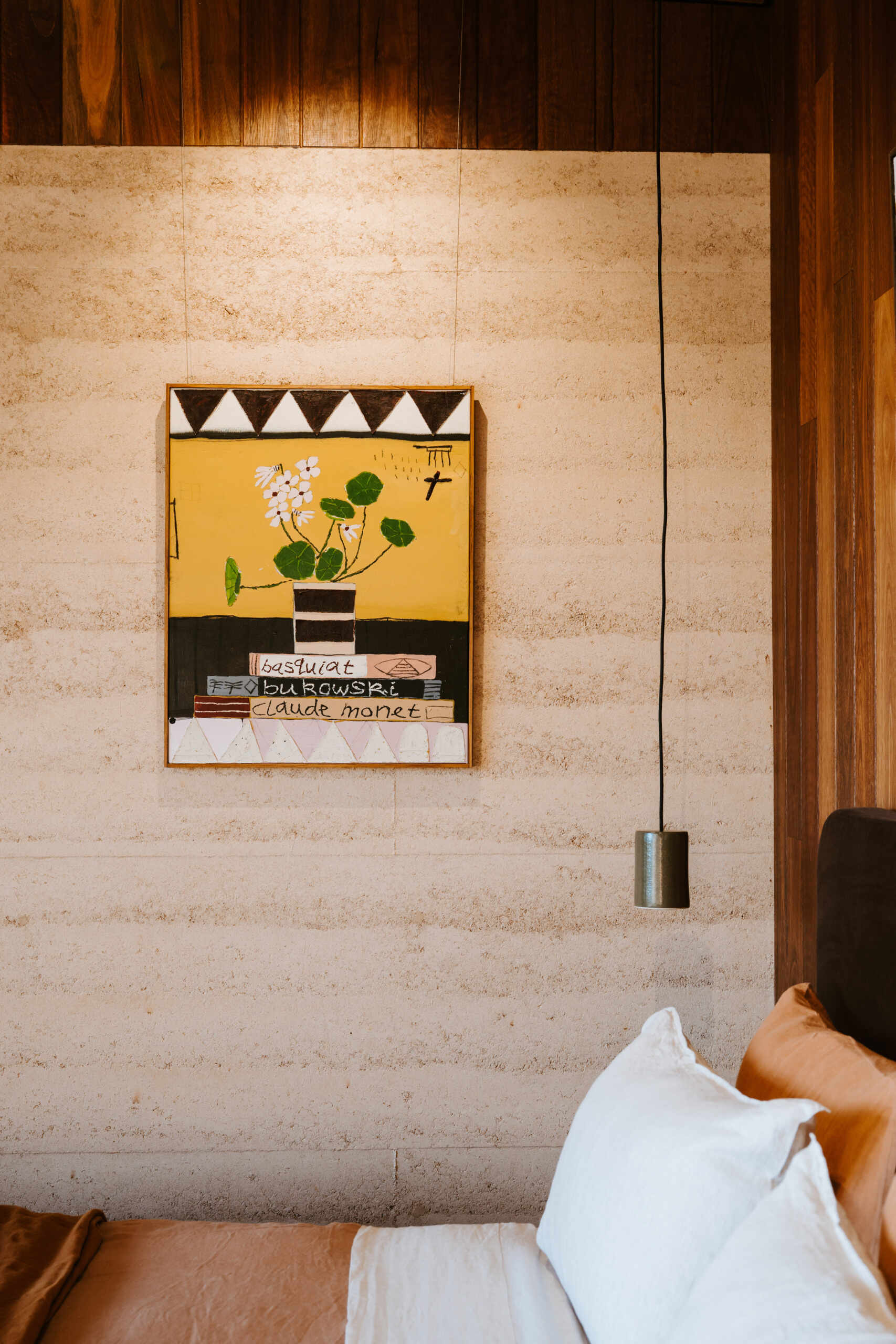 A contemporary off-grid cabin in Mudgee with an open-plan layout that combines the living area, bedroom, and kitchen into one light-filled space. Rammed earth walls, warm timber finishes, a minimalist bathroom, and an outdoor bathtub overlooking the landscape create a relaxing vineyard farm stay surrounded by Australian art and valley views.