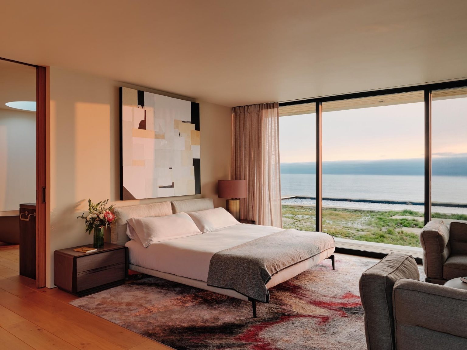 The main bedroom continues the home’s modern yet comfortable aesthetic. Soft textures and a large rug introduce warmth and color, while the restrained material palette keeps the room feeling calm and uncluttered.