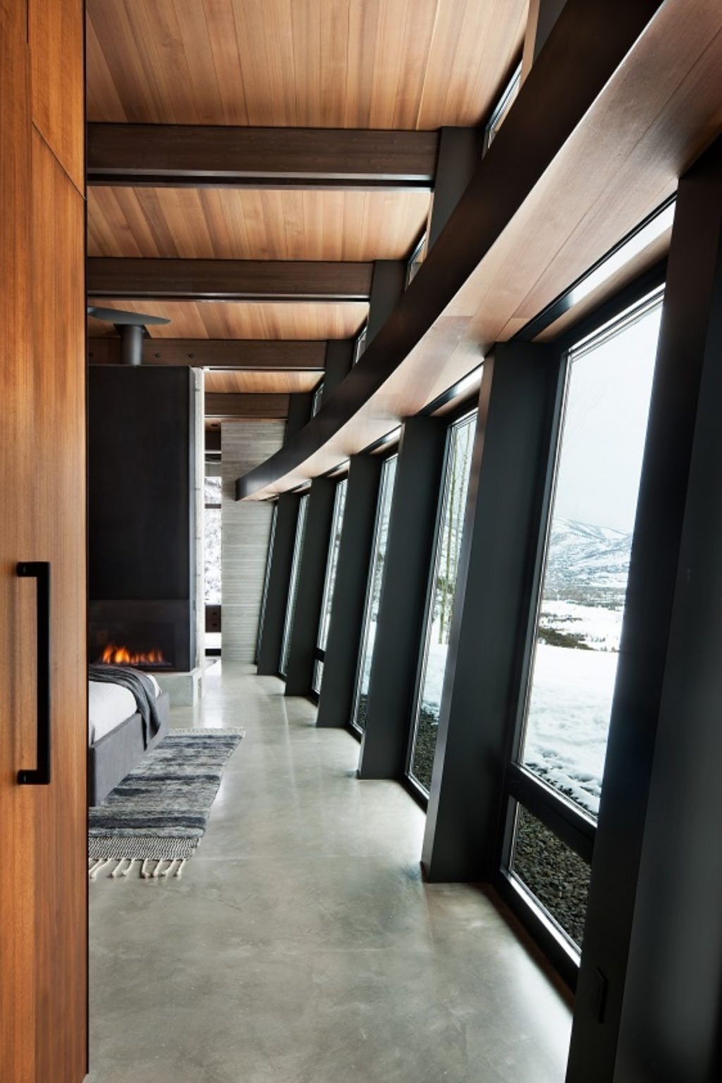 The home's signature outward-leaning glass wall is especially dramatic in this bedroom. The angled glazing expands the sense of space while framing uninterrupted views of the surrounding mountain landscape.