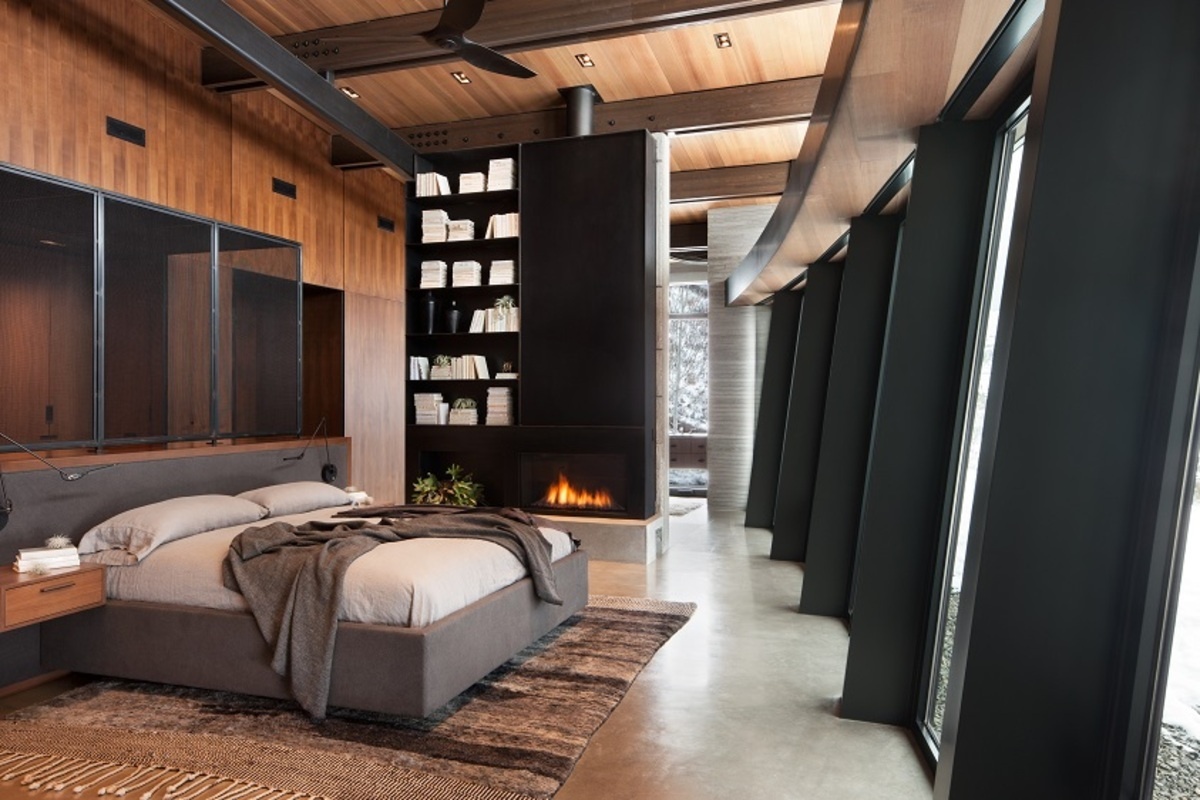 Exposed steel structure, black shelving, and a dark fireplace create a bold architectural statement in this bedroom. The contrast between industrial materials and warm finishes adds depth and character to the interior.
