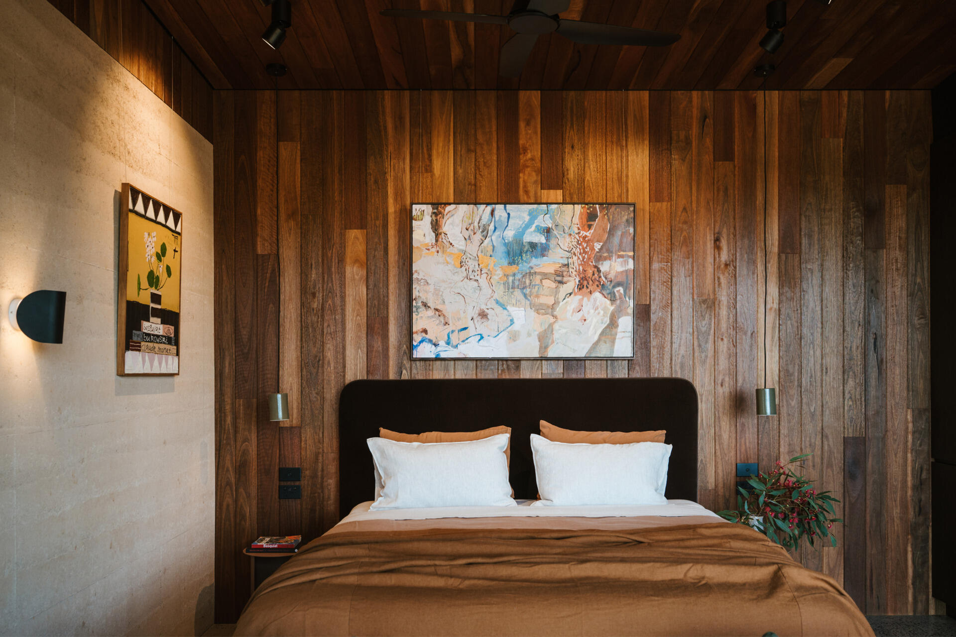 A contemporary off-grid cabin in Mudgee with an open-plan layout that combines the living area, bedroom, and kitchen into one light-filled space. Rammed earth walls, warm timber finishes, a minimalist bathroom, and an outdoor bathtub overlooking the landscape create a relaxing vineyard farm stay surrounded by Australian art and valley views.