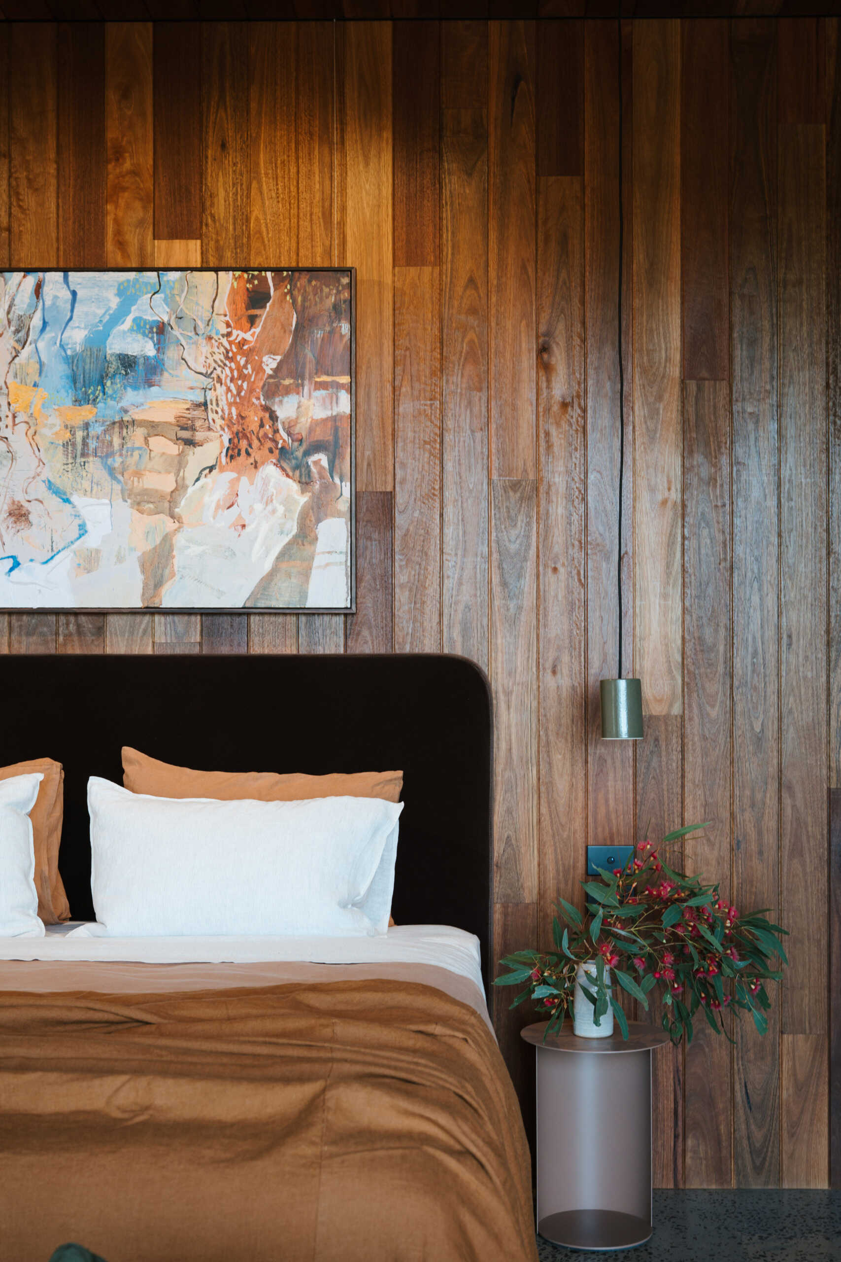 A contemporary off-grid cabin in Mudgee with an open-plan layout that combines the living area, bedroom, and kitchen into one light-filled space. Rammed earth walls, warm timber finishes, a minimalist bathroom, and an outdoor bathtub overlooking the landscape create a relaxing vineyard farm stay surrounded by Australian art and valley views.