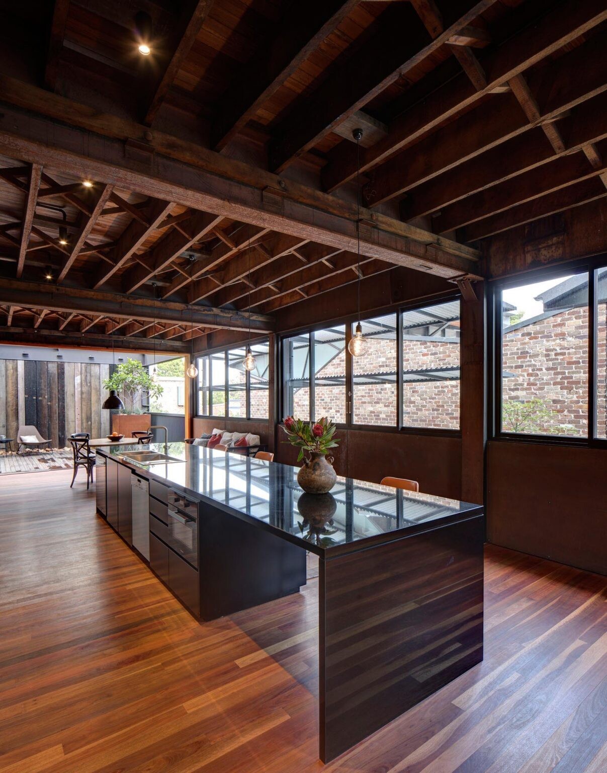 Matte black cabinetry, mirrored surfaces, and sliding glass doors define the kitchen, opening into a courtyard filled with reclaimed beams, stone, and recycled brick water features.