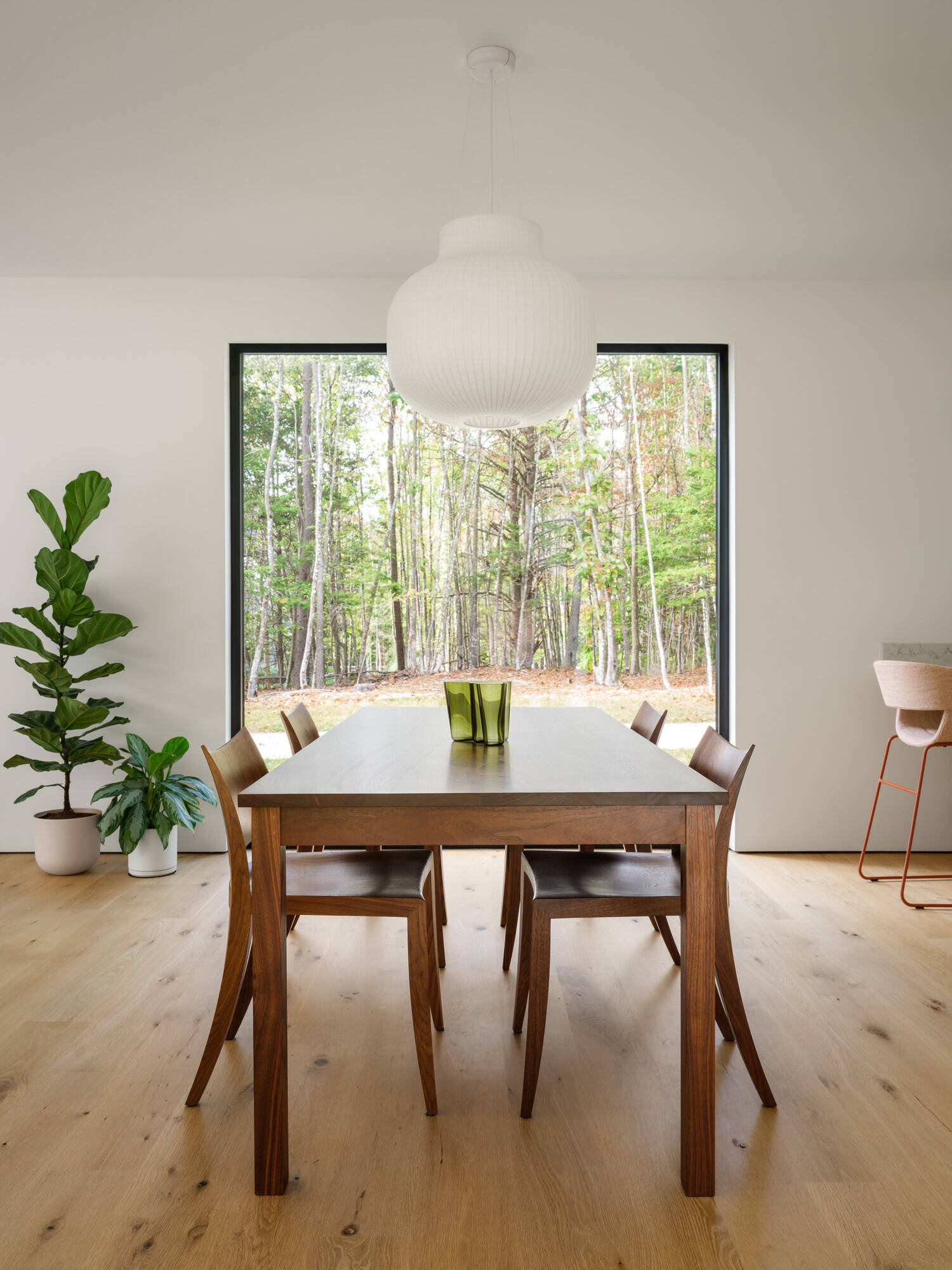 This bright kitchen and dining space connects seamlessly to a screened porch and surrounding forest views in rural Maine.