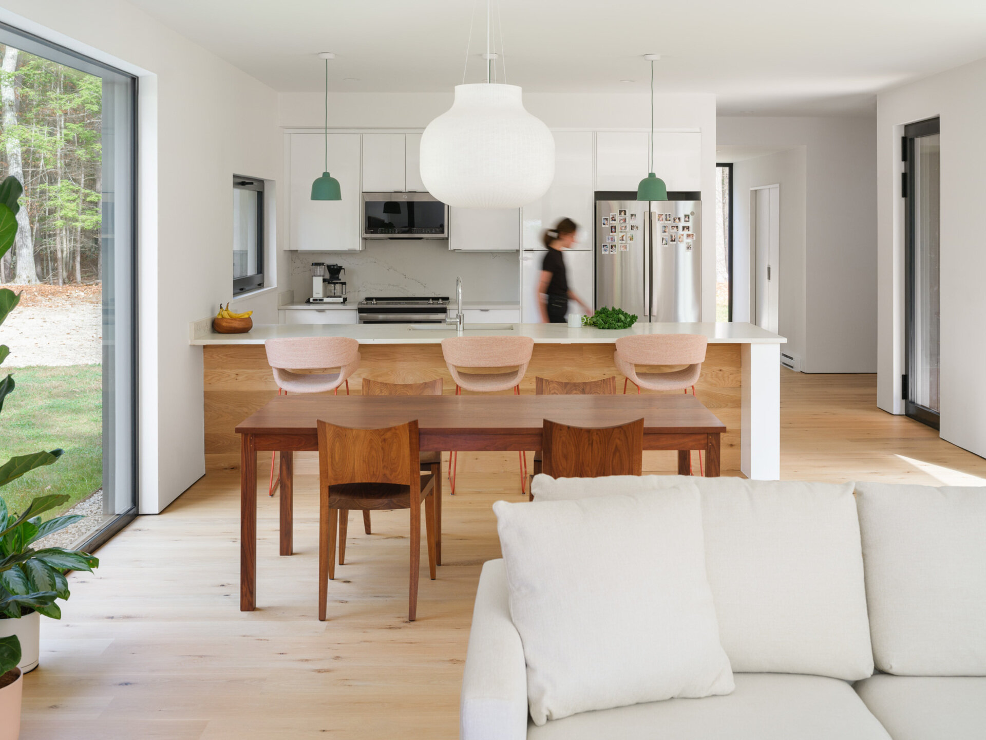 This bright kitchen and dining space connects seamlessly to a screened porch and surrounding forest views in rural Maine.