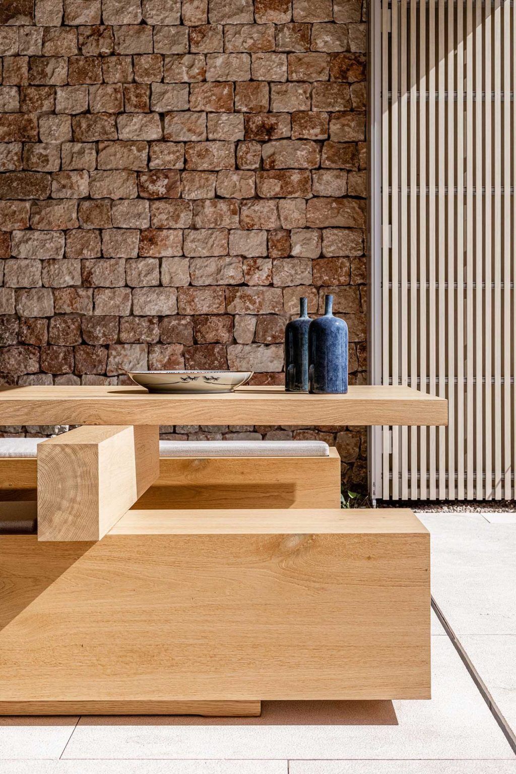 A minimalist kitchen with wood cabinetry and sliding glass walls opens directly onto a covered outdoor dining space in Mallorca.