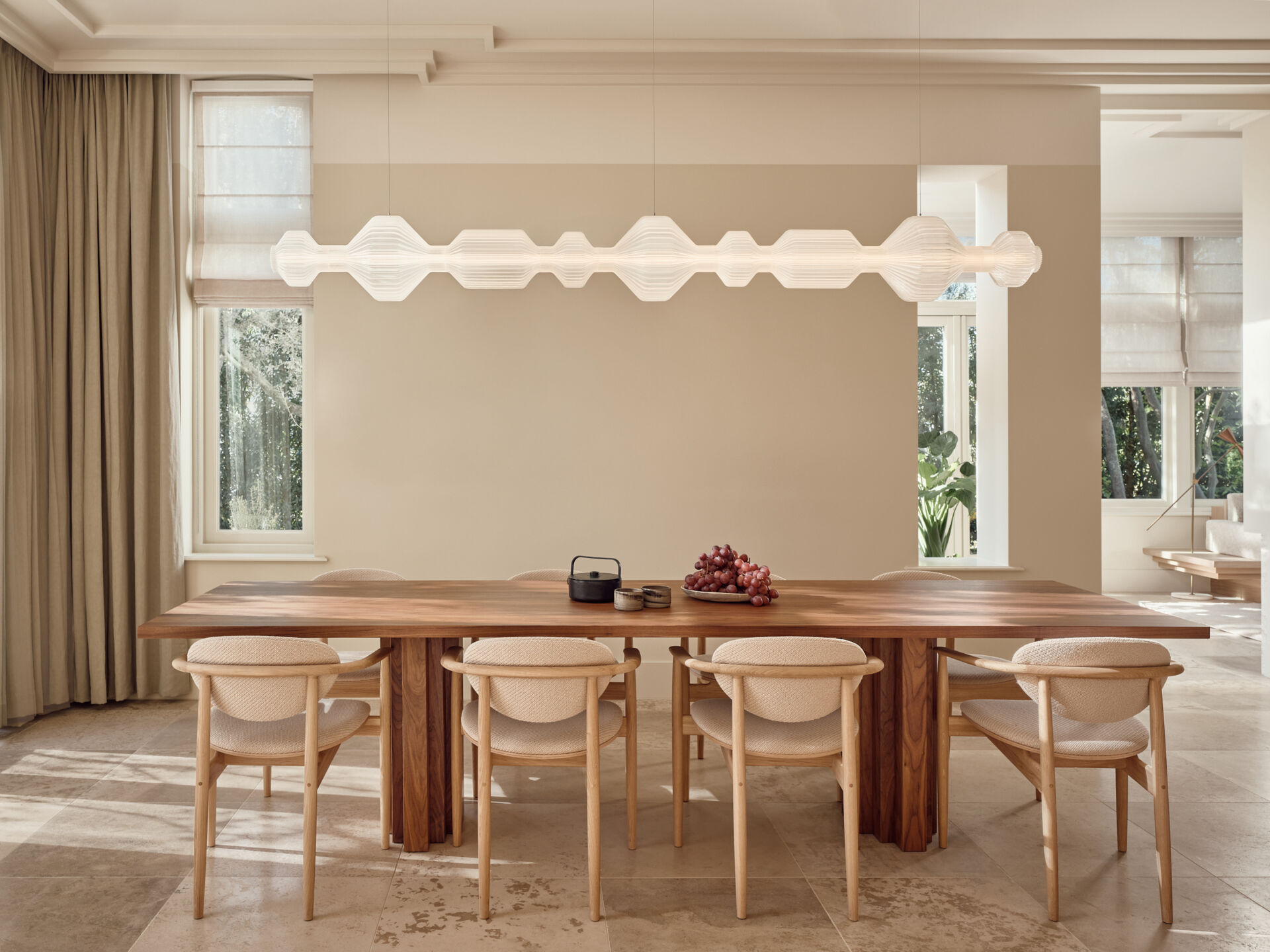 This elegant dining space pairs a dark walnut table with soft neutral interiors and open views toward the kitchen and garden.