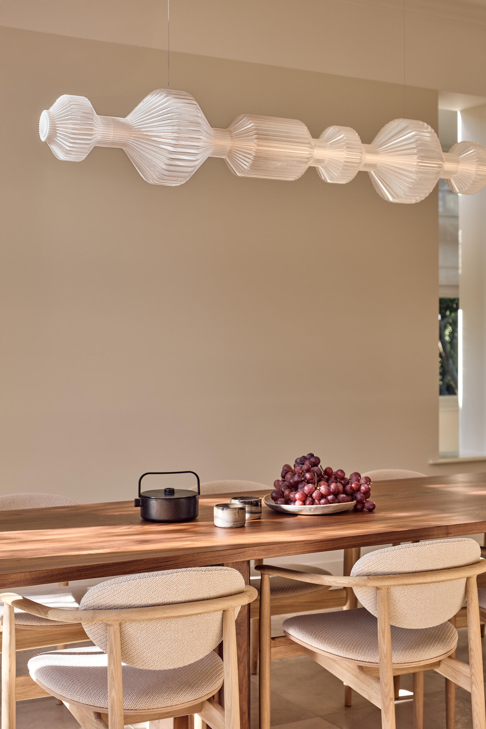 This elegant dining space pairs a dark walnut table with soft neutral interiors and open views toward the kitchen and garden.
