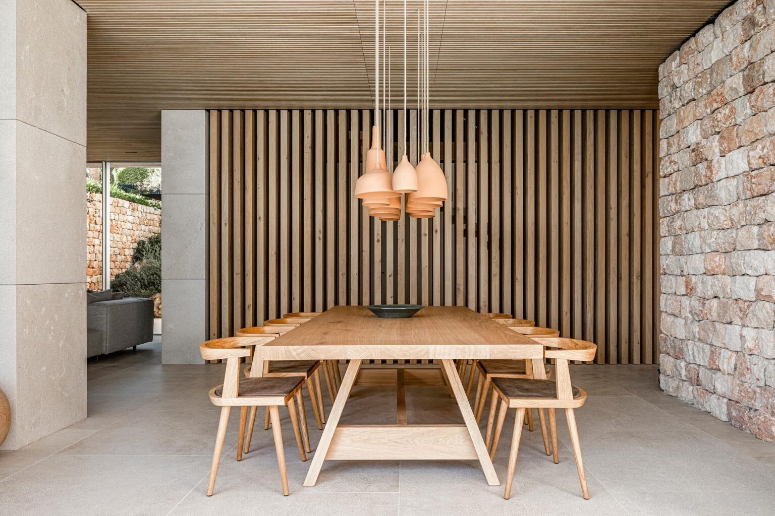 In the open-plan living and dining area, natural textures soften the modern architecture. Above the dining table, a cluster of handmade ceramic pendant lights creates a sculptural centerpiece while adding warmth to the room.