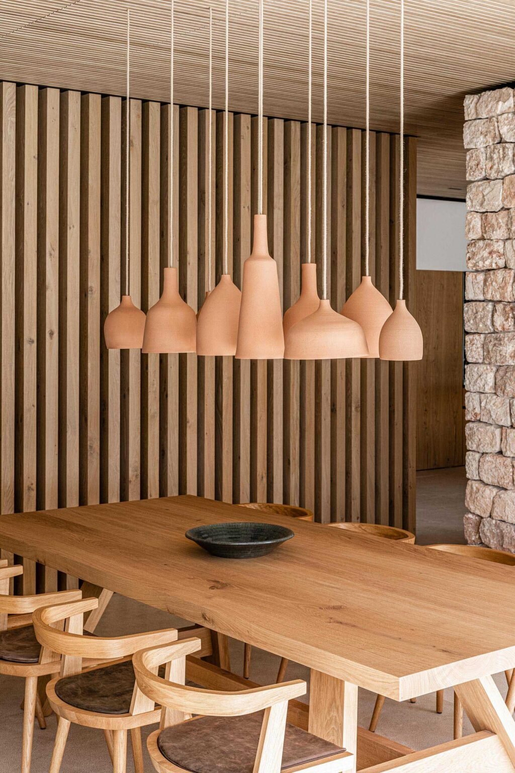 In the open-plan living and dining area, natural textures soften the modern architecture. Above the dining table, a cluster of handmade ceramic pendant lights creates a sculptural centerpiece while adding warmth to the room.
