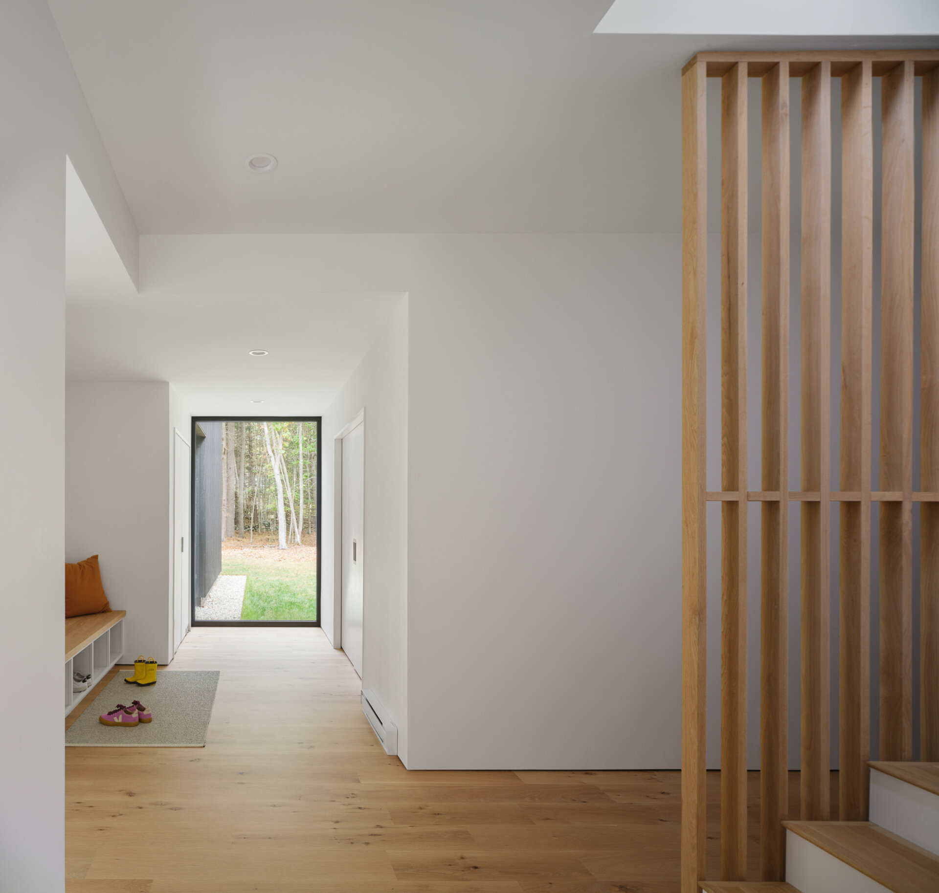 A covered porch, warm ash finishes, and natural light make the entryway of this Maine home feel welcoming and bright.