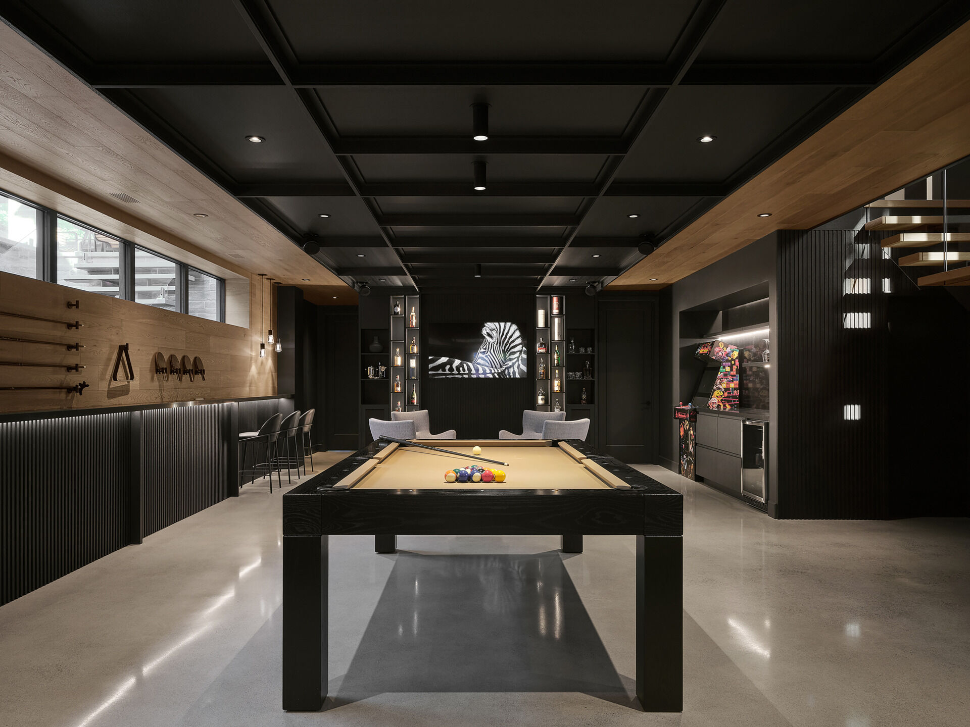 On the lower level, the games room, with its lounge area, pool table, kitchenette, and storage, benefits from the natural slope of the terrain, with a line of windows helping the space to feel bright and visually open despite being partially below grade. 