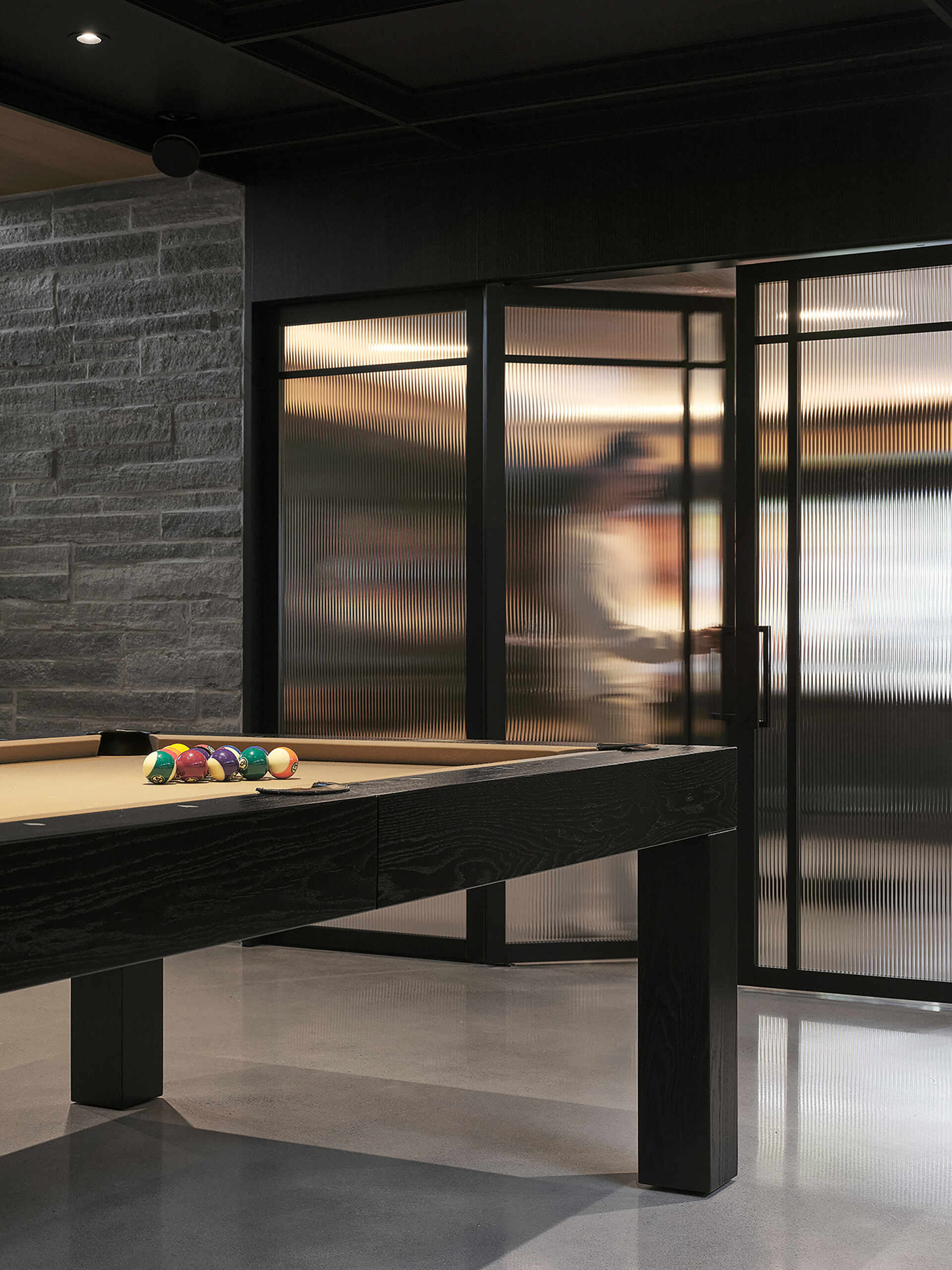 On the lower level, the games room, with its lounge area, pool table, kitchenette, and storage, benefits from the natural slope of the terrain, with a line of windows helping the space to feel bright and visually open despite being partially below grade. 