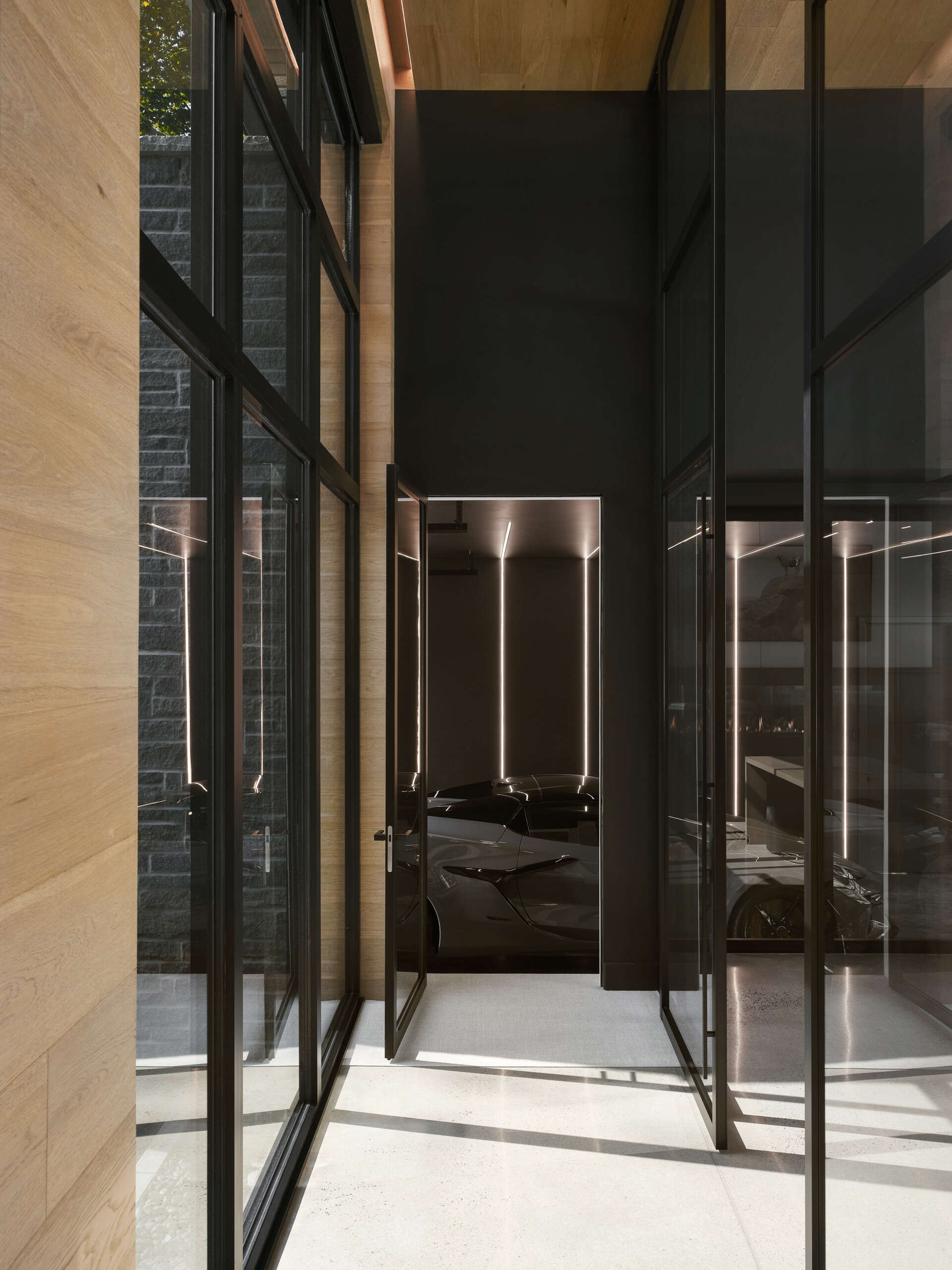 The garage is a dramatic moment in the home, with its black walls, ceiling, and floors highlighted by integrated lighting, making the car appear as a sculptural element.