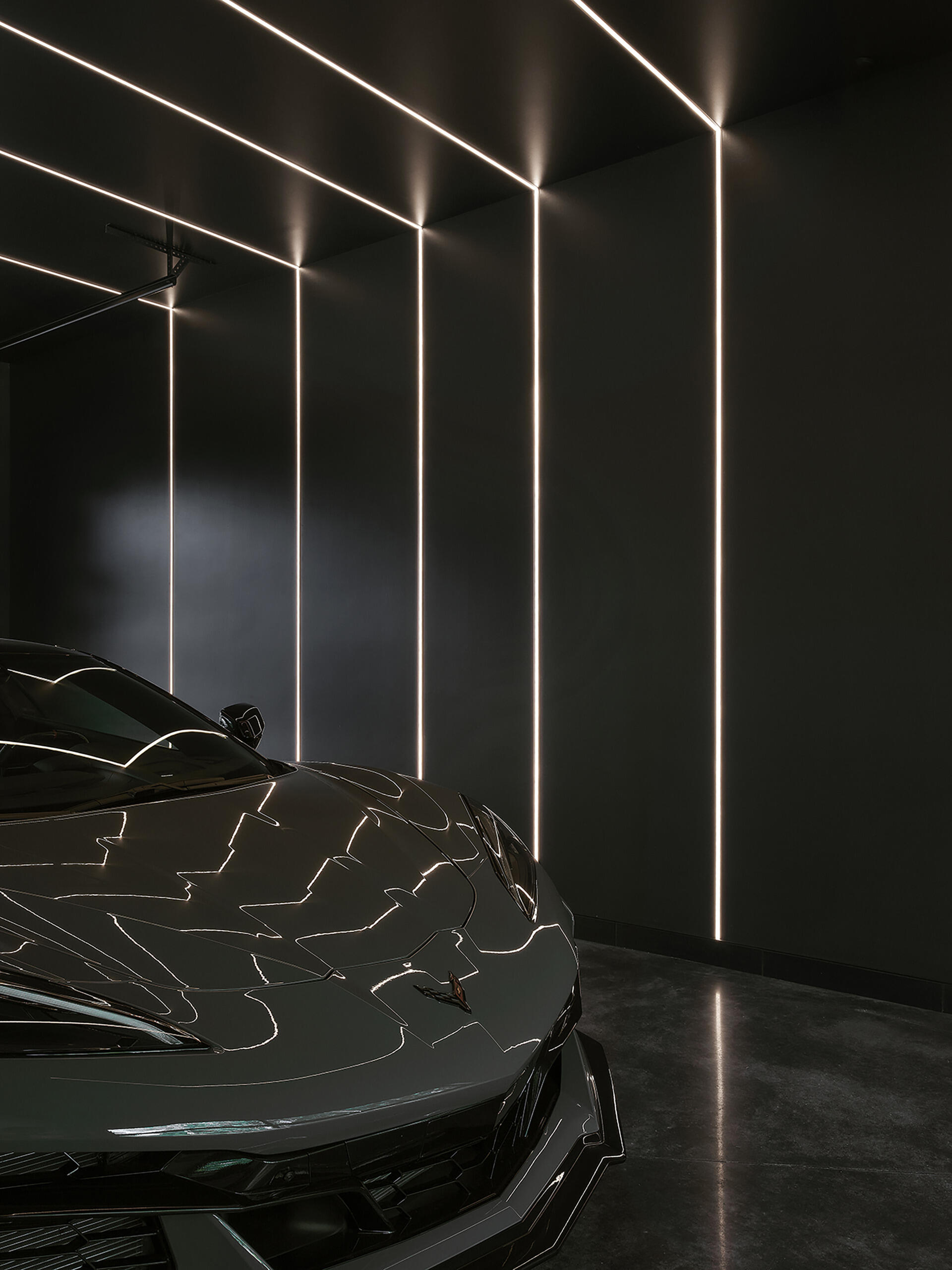 The garage is a dramatic moment in the home, with its black walls, ceiling, and floors highlighted by integrated lighting, making the car appear as a sculptural element.