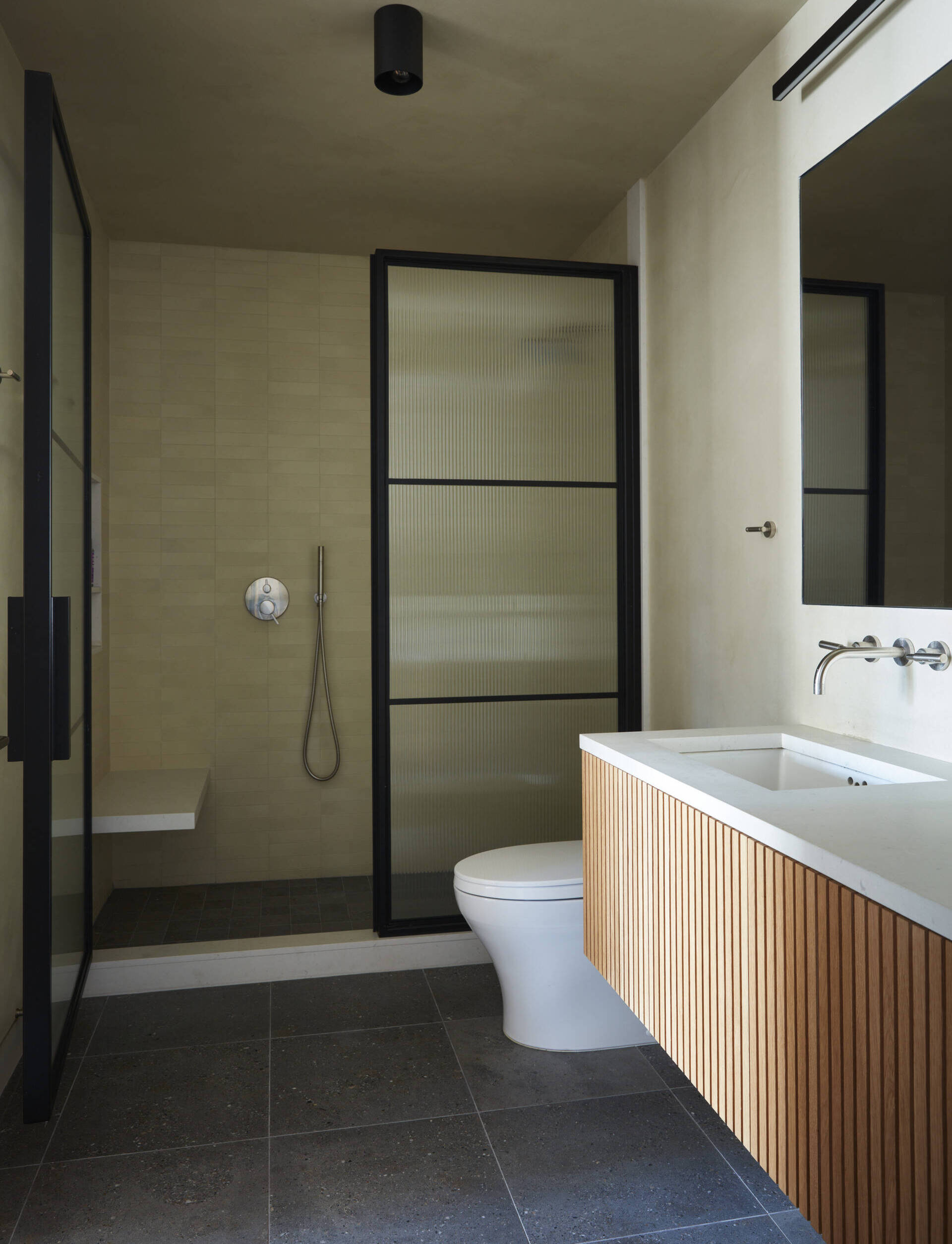 Venetian plaster walls, ribbed glass, and blackened steel details create a dramatic modern bathroom.