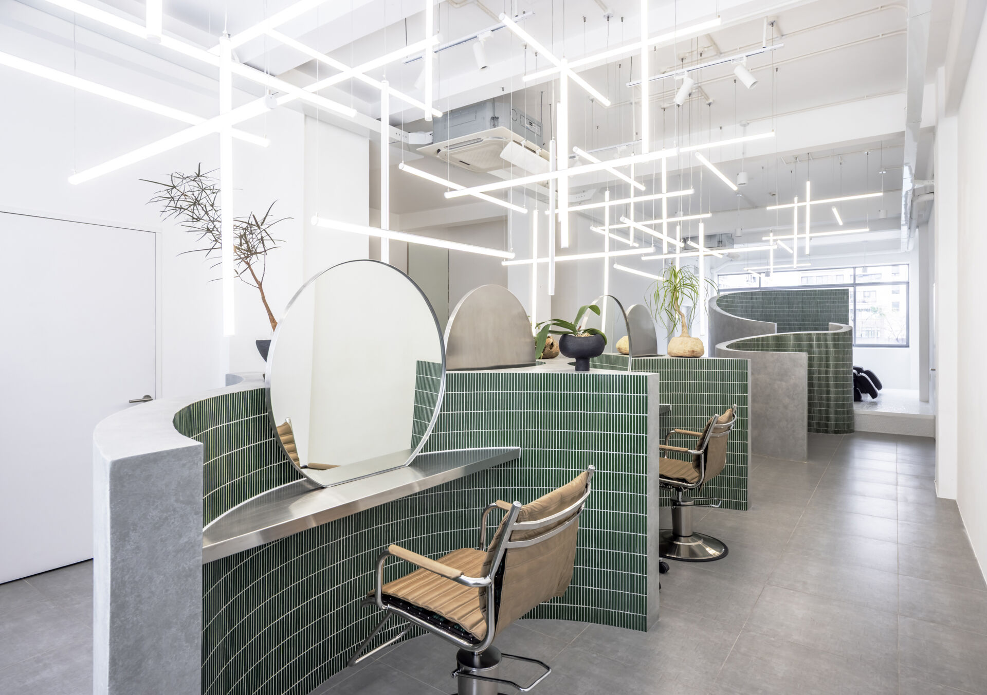 A hair salon in Ho Chi Minh City designed by Inrestudio, shaped by a continuous sculptural wall that guides movement through waiting areas, styling stations, and shampoo spaces. The interior shifts between green tile and raw grey surfaces, with light and form changing as you move through each level of the maisonette.