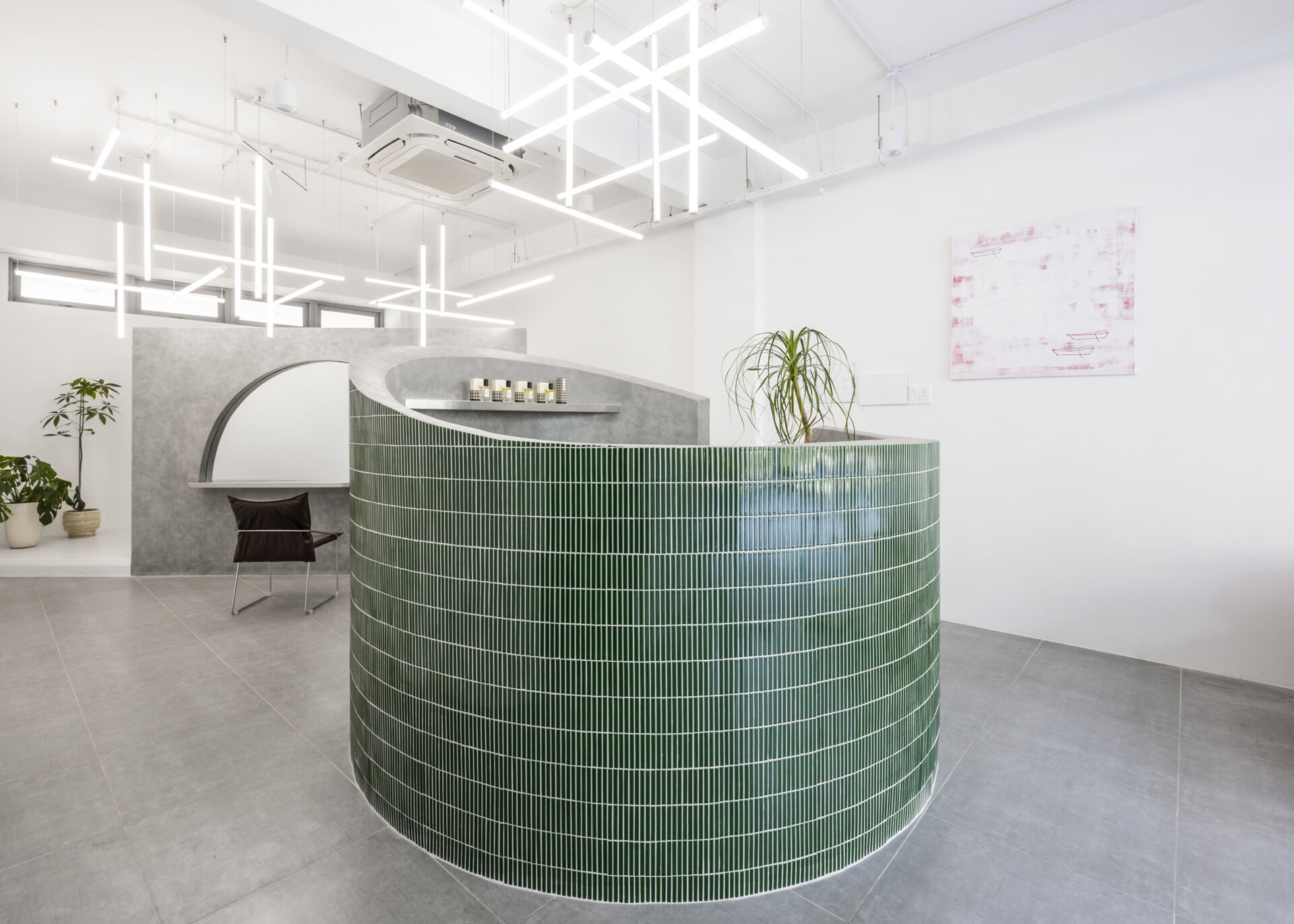 A hair salon in Ho Chi Minh City designed by Inrestudio, shaped by a continuous sculptural wall that guides movement through waiting areas, styling stations, and shampoo spaces. The interior shifts between green tile and raw grey surfaces, with light and form changing as you move through each level of the maisonette.