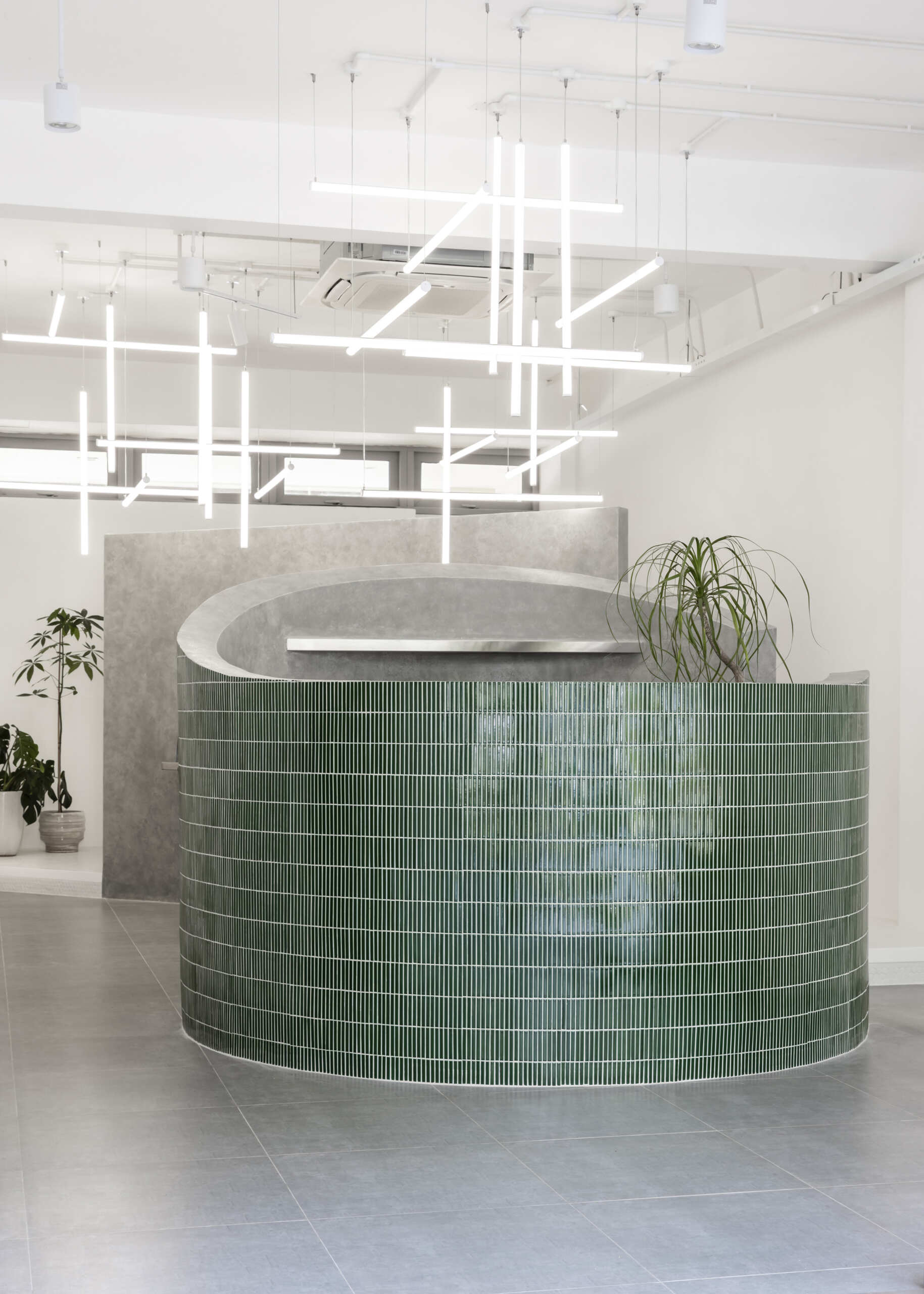 A hair salon in Ho Chi Minh City designed by Inrestudio, shaped by a continuous sculptural wall that guides movement through waiting areas, styling stations, and shampoo spaces. The interior shifts between green tile and raw grey surfaces, with light and form changing as you move through each level of the maisonette.