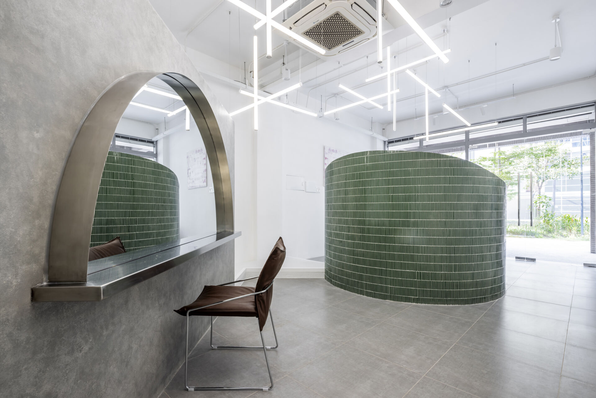 A hair salon in Ho Chi Minh City designed by Inrestudio, shaped by a continuous sculptural wall that guides movement through waiting areas, styling stations, and shampoo spaces. The interior shifts between green tile and raw grey surfaces, with light and form changing as you move through each level of the maisonette.