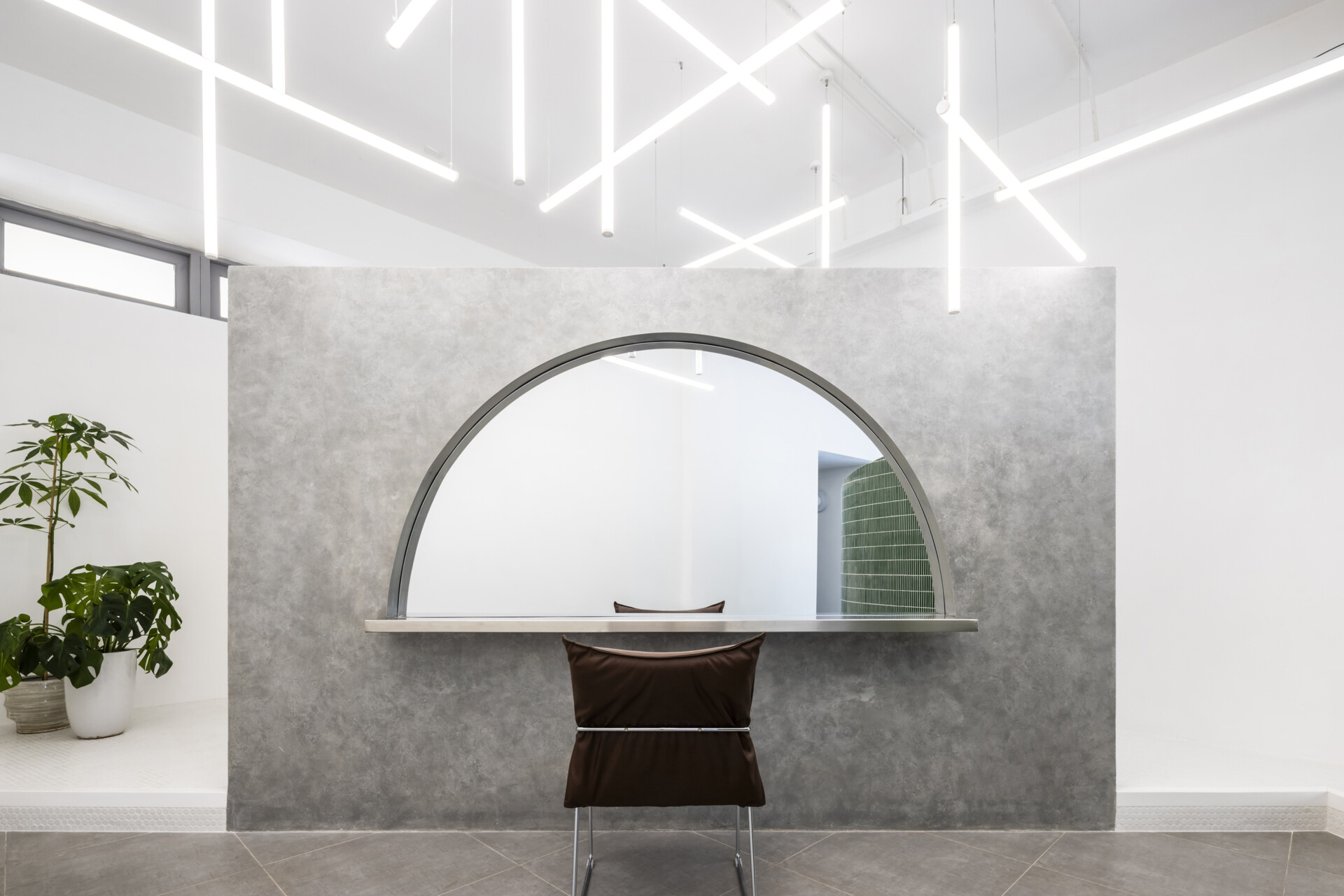 A hair salon in Ho Chi Minh City designed by Inrestudio, shaped by a continuous sculptural wall that guides movement through waiting areas, styling stations, and shampoo spaces. The interior shifts between green tile and raw grey surfaces, with light and form changing as you move through each level of the maisonette.