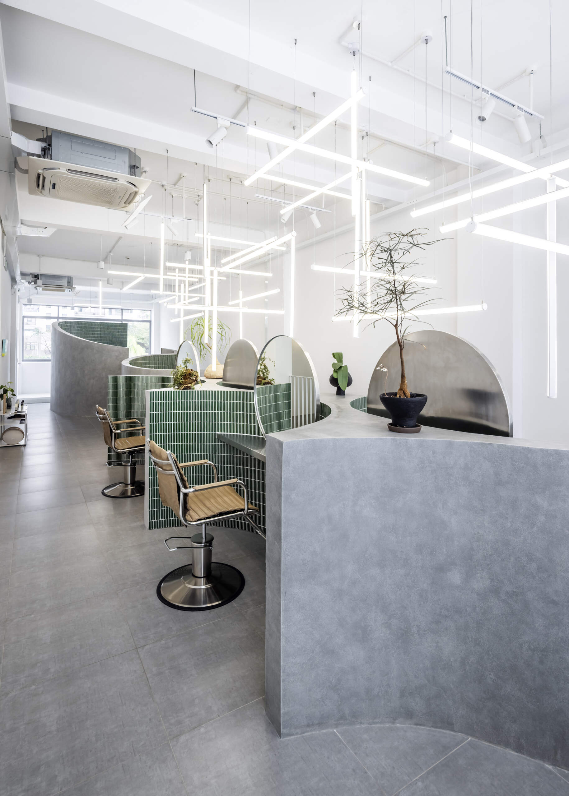 A hair salon in Ho Chi Minh City designed by Inrestudio, shaped by a continuous sculptural wall that guides movement through waiting areas, styling stations, and shampoo spaces. The interior shifts between green tile and raw grey surfaces, with light and form changing as you move through each level of the maisonette.