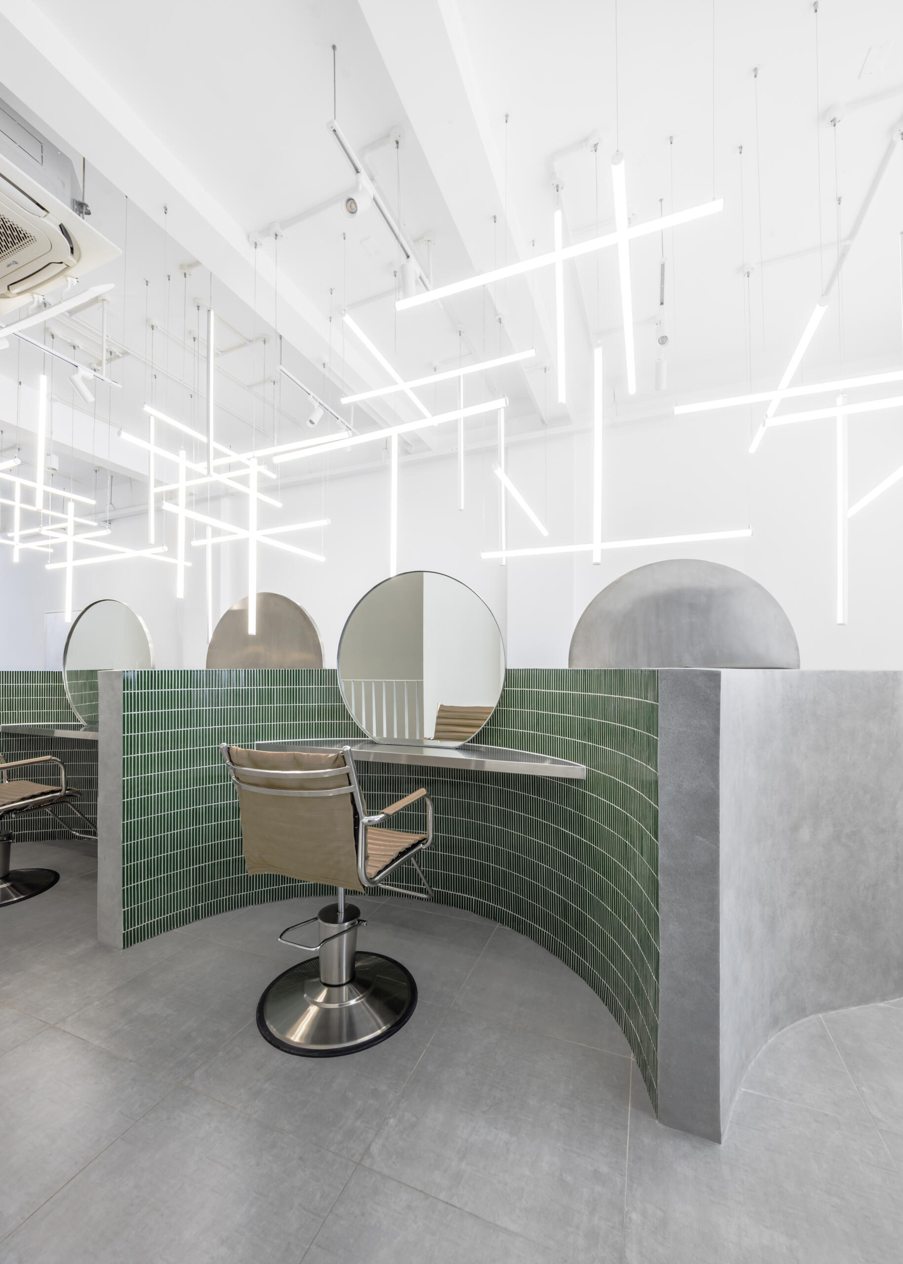 A hair salon in Ho Chi Minh City designed by Inrestudio, shaped by a continuous sculptural wall that guides movement through waiting areas, styling stations, and shampoo spaces. The interior shifts between green tile and raw grey surfaces, with light and form changing as you move through each level of the maisonette.