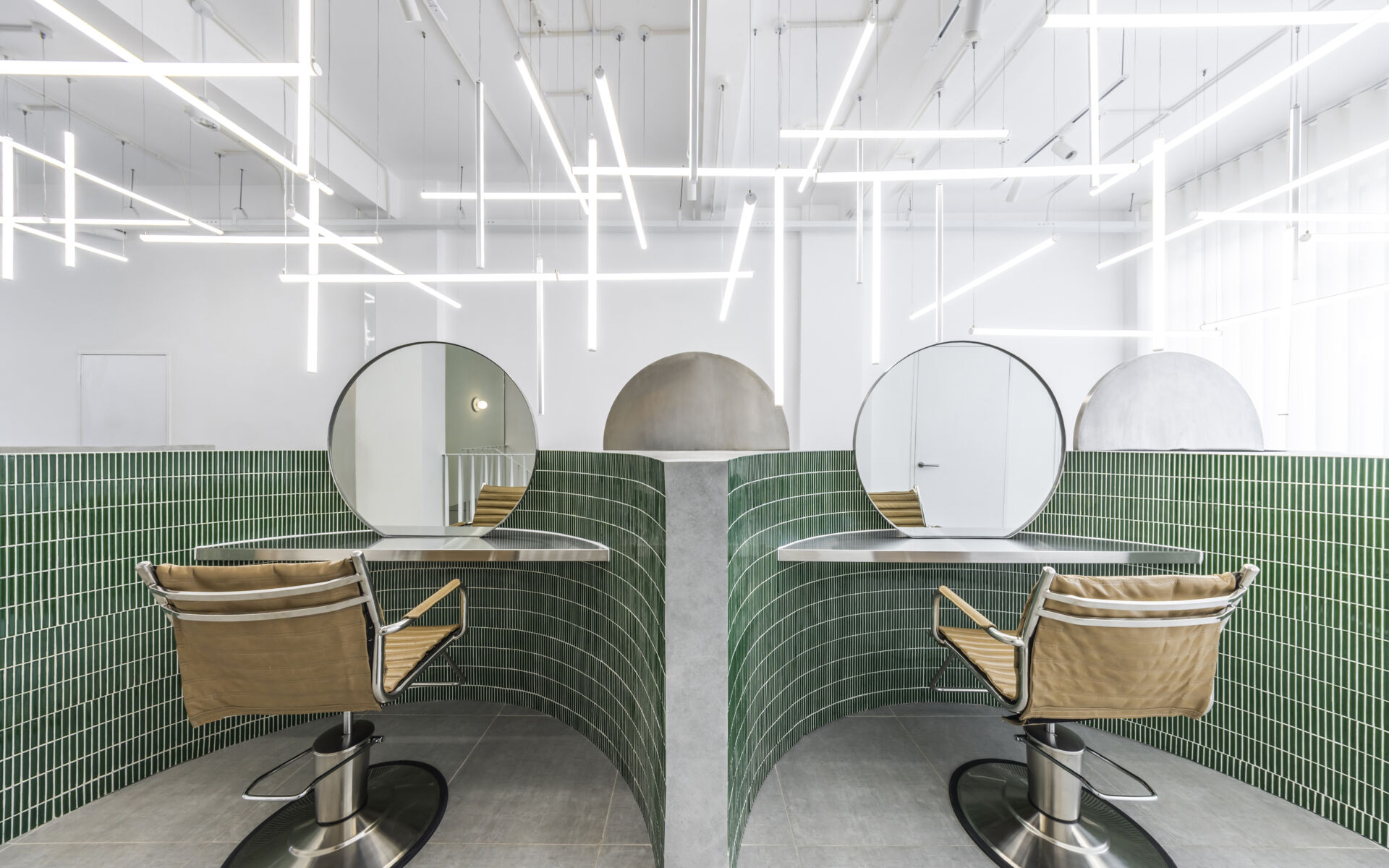 A hair salon in Ho Chi Minh City designed by Inrestudio, shaped by a continuous sculptural wall that guides movement through waiting areas, styling stations, and shampoo spaces. The interior shifts between green tile and raw grey surfaces, with light and form changing as you move through each level of the maisonette.