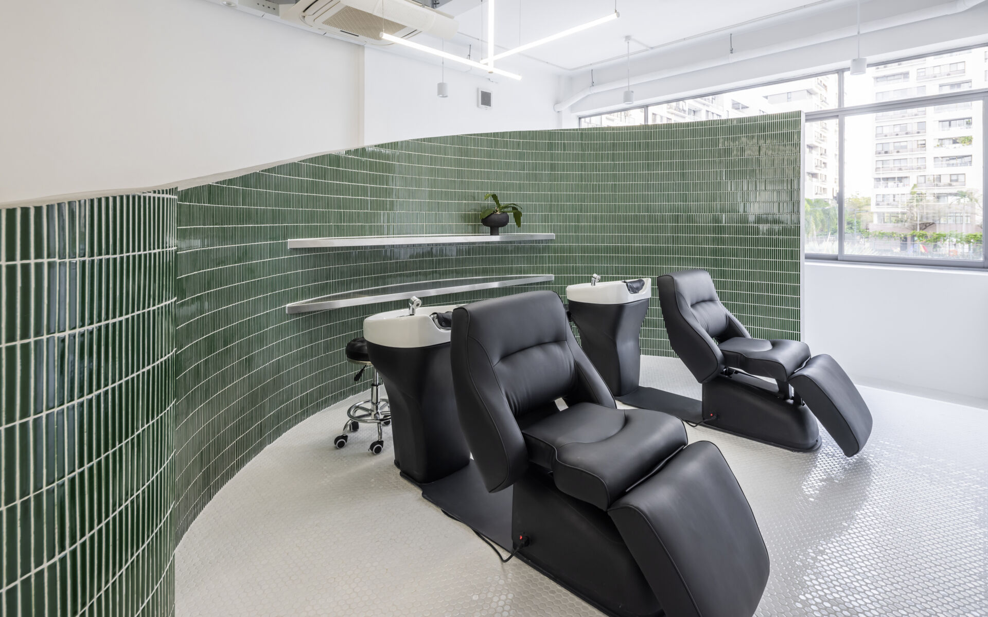 A hair salon in Ho Chi Minh City designed by Inrestudio, shaped by a continuous sculptural wall that guides movement through waiting areas, styling stations, and shampoo spaces. The interior shifts between green tile and raw grey surfaces, with light and form changing as you move through each level of the maisonette.