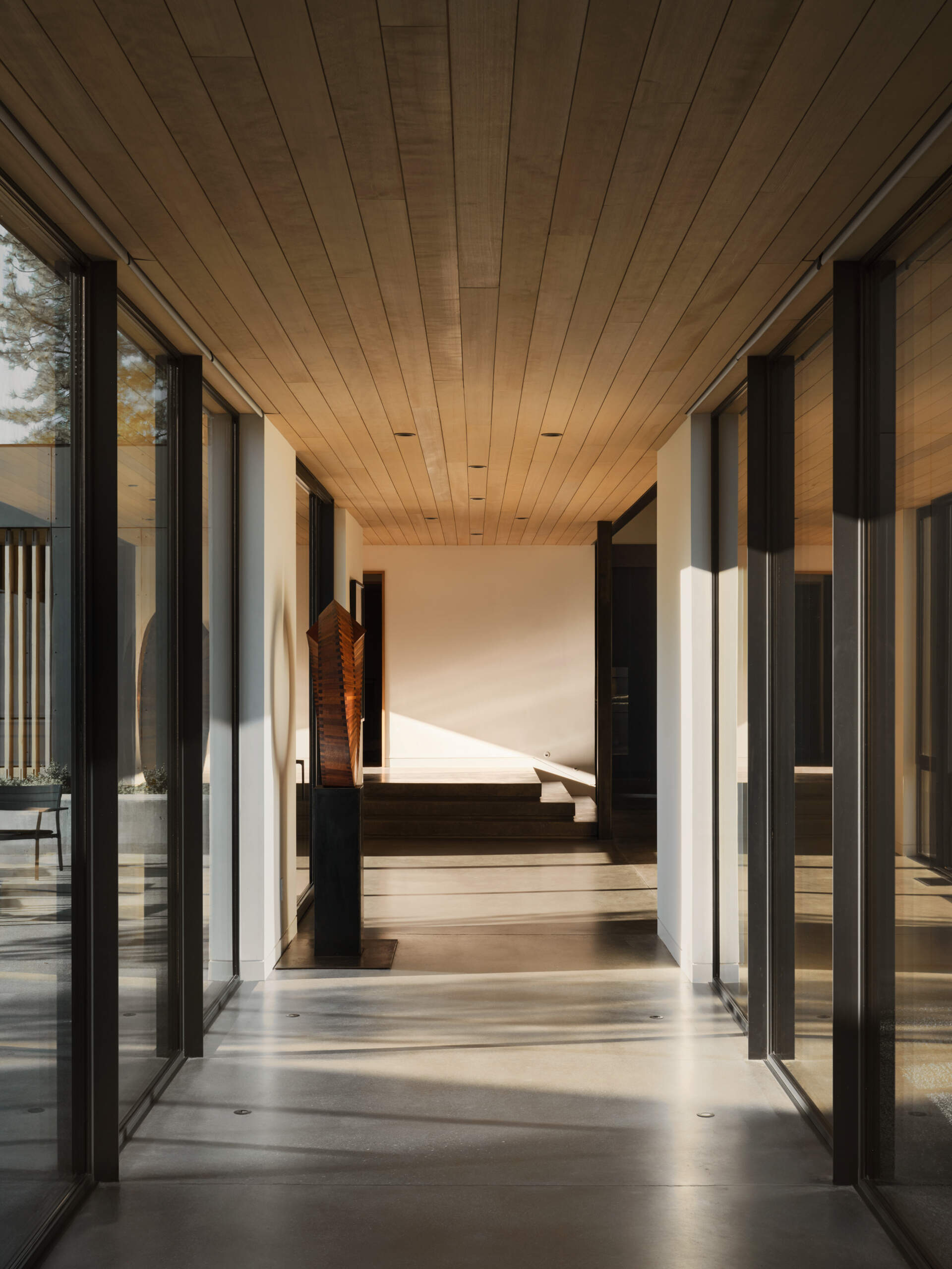 This glass-lined hallway acts like a viewing gallery, framing peaceful forest views from every angle inside the home.