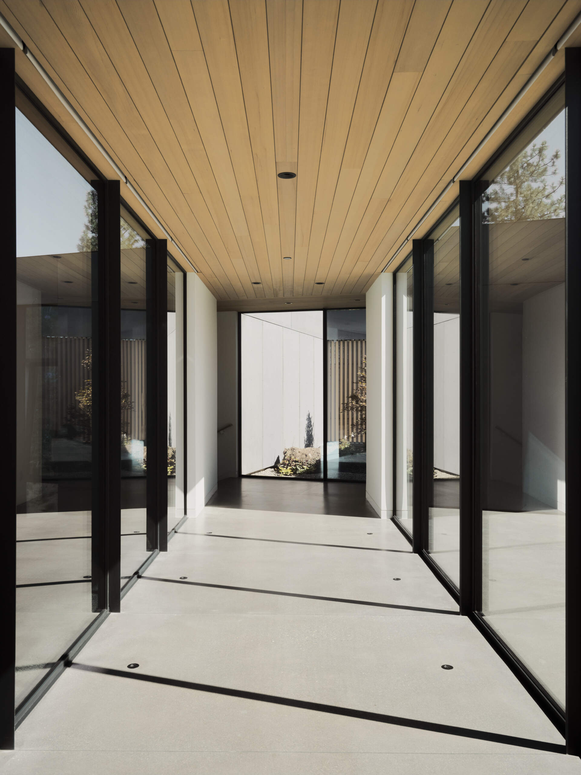 This glass-lined hallway acts like a viewing gallery, framing peaceful forest views from every angle inside the home.