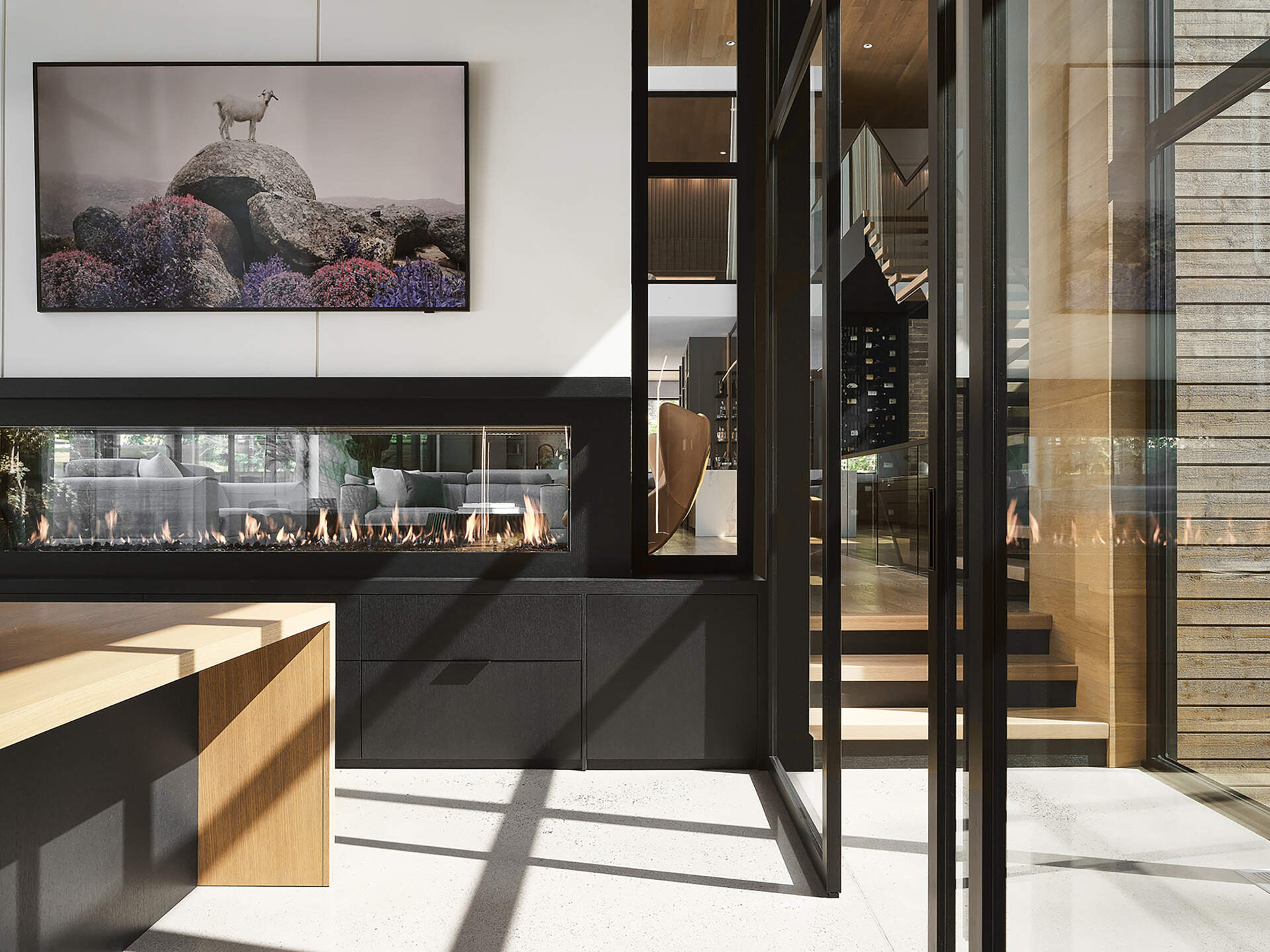 Positioned on the other side of the double-sided fireplace in the living room, the home office feels calm and visually open, with glass walls keeping it bright and connected to the other interior spaces.
