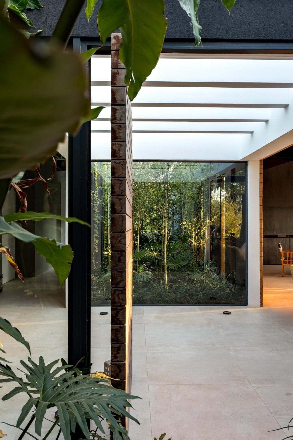 A tropical-lined pathway leads to a pivoting front door, where glass walls frame garden views and introduce the home’s split layout.