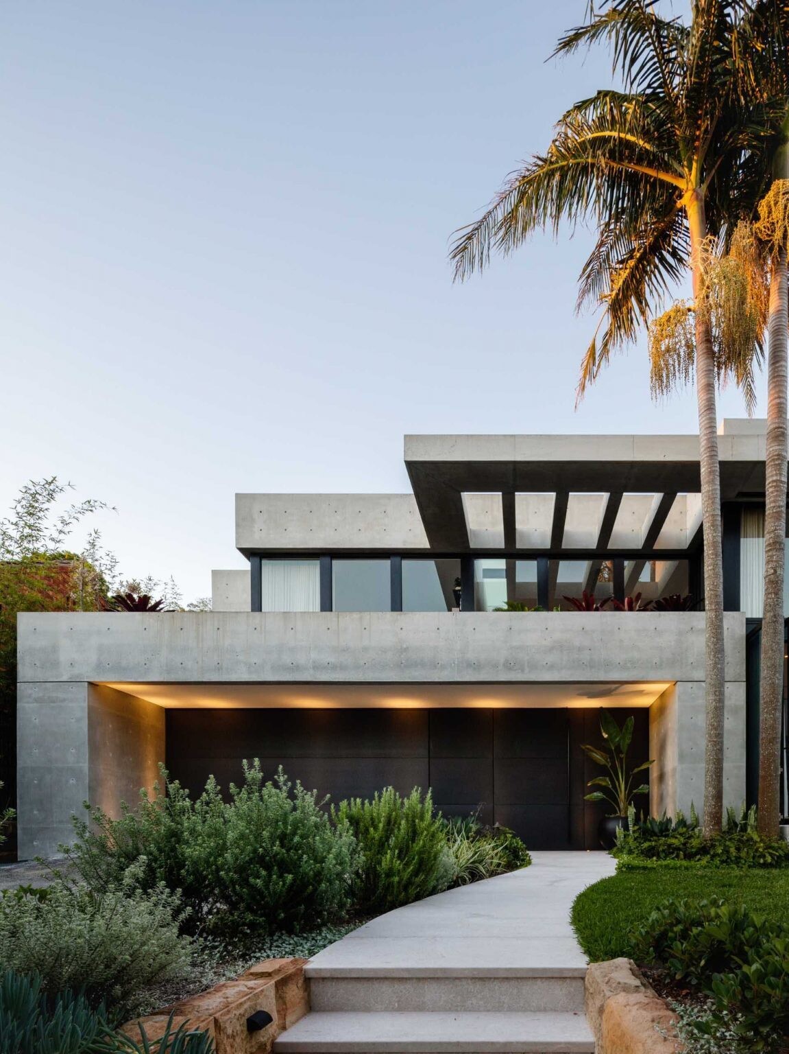 This modern Sydney home by Manolev Architects was designed around towering Bangalow palms, with a curved garden path and floating concrete deck creating a dramatic first impression.