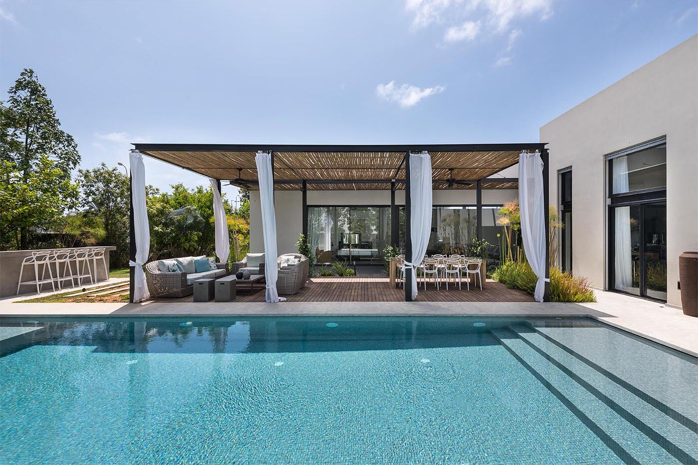 This modern home by Neuman Hayner Architects combines bamboo pergolas, minimalist interiors, and multiple outdoor entertaining spaces connected through shaded pathways.