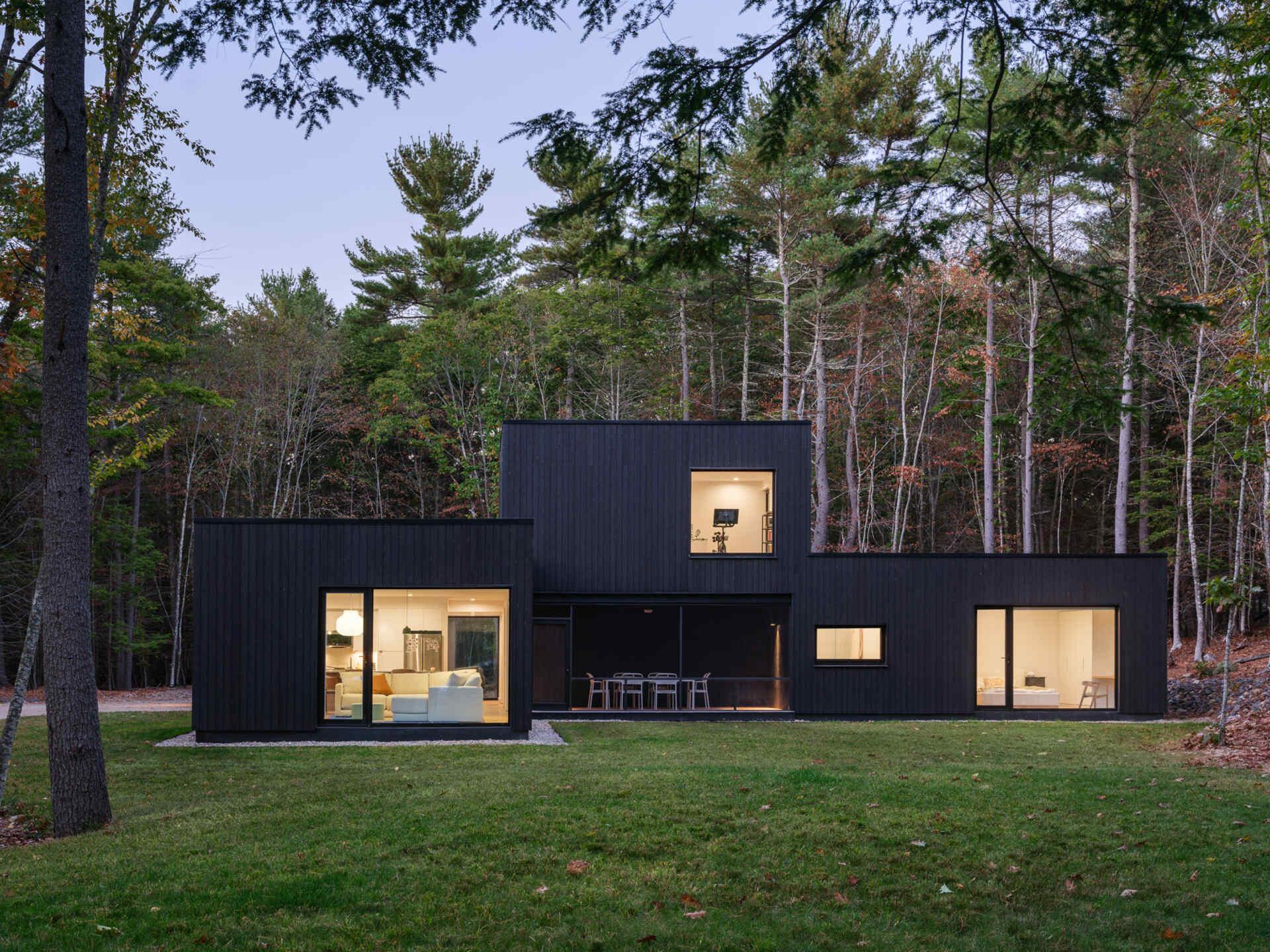 This Maine home uses black charred wood siding and dramatic floor-to-ceiling glass to create a modern exterior in the forest.