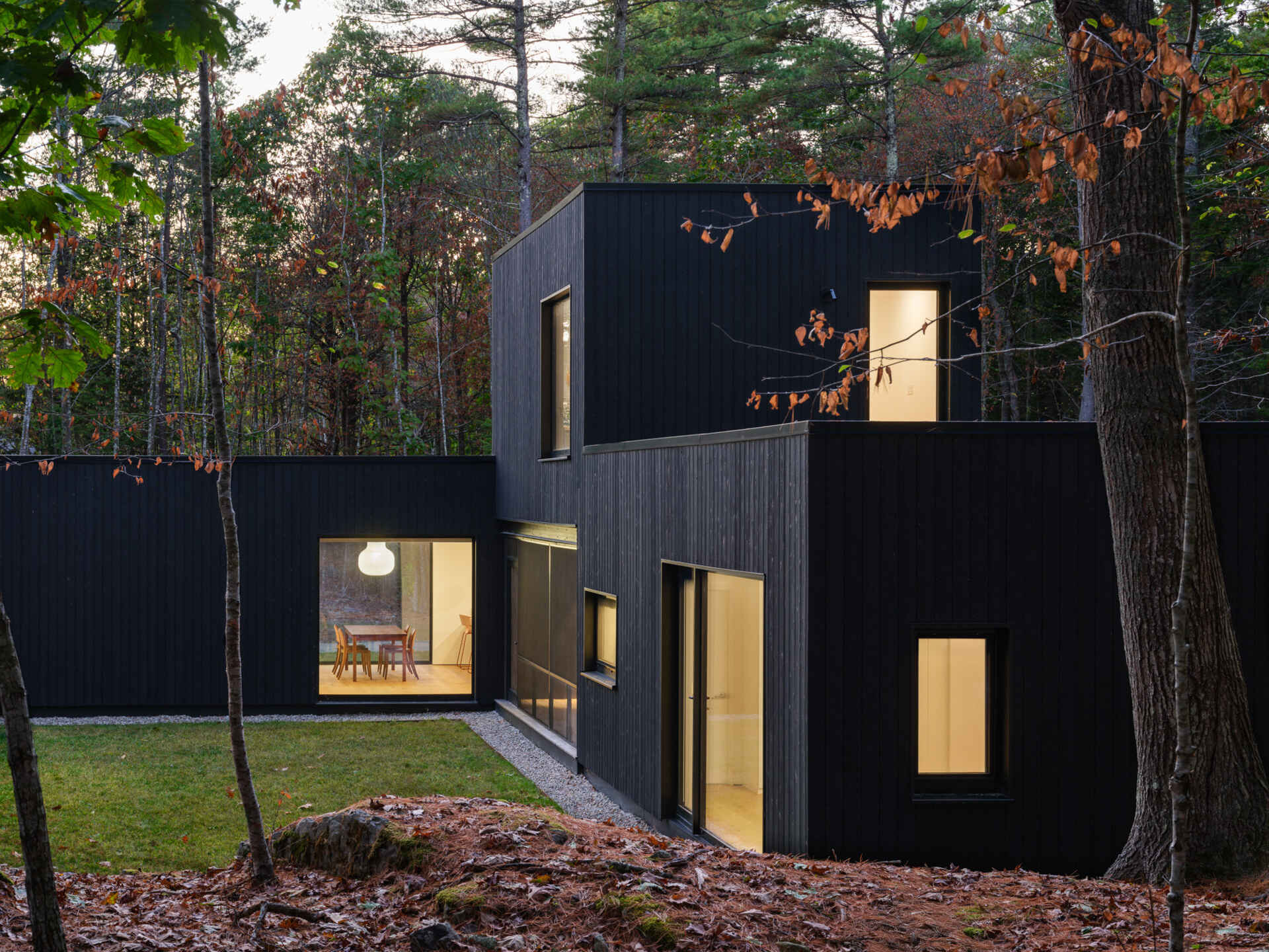 This Maine home uses black charred wood siding and dramatic floor-to-ceiling glass to create a modern exterior in the forest.