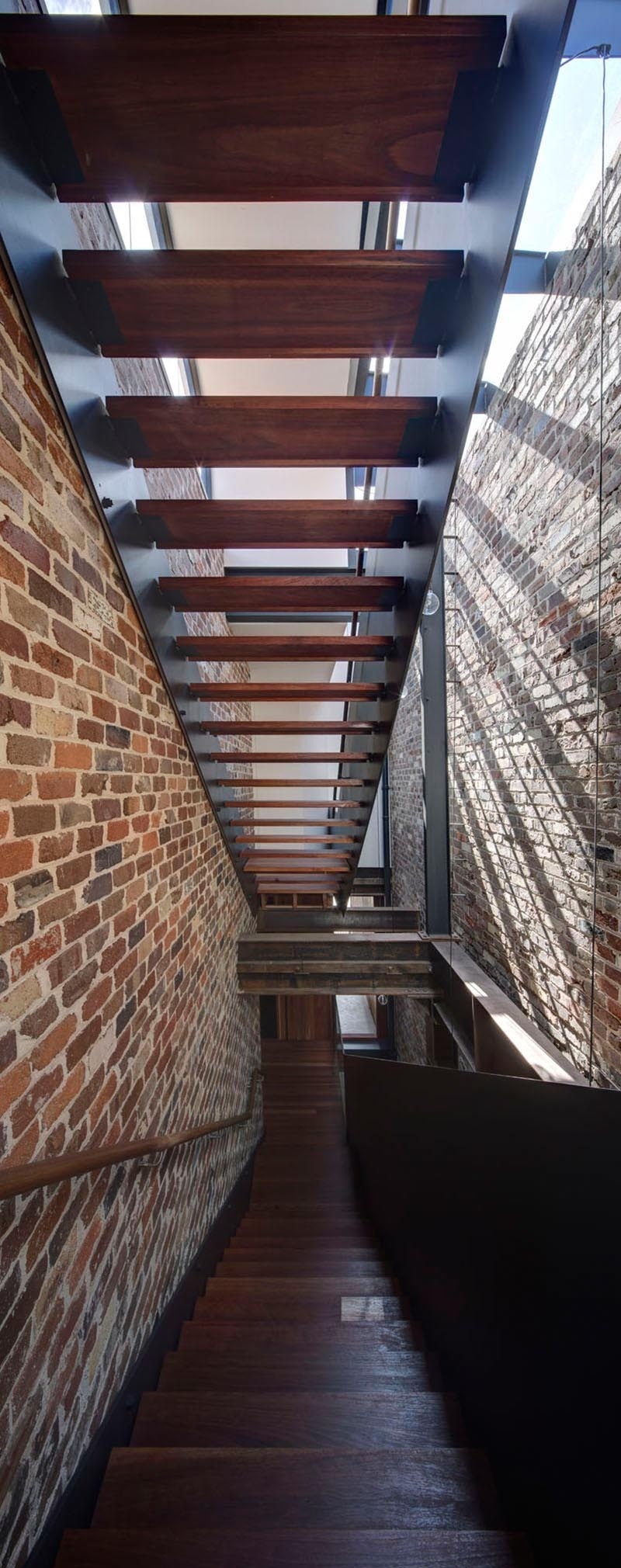 A dramatic four-storey brick wall runs alongside a skylit staircase, with exposed steel beams and a 12-metre void bringing natural light deep into this Sydney warehouse conversion.